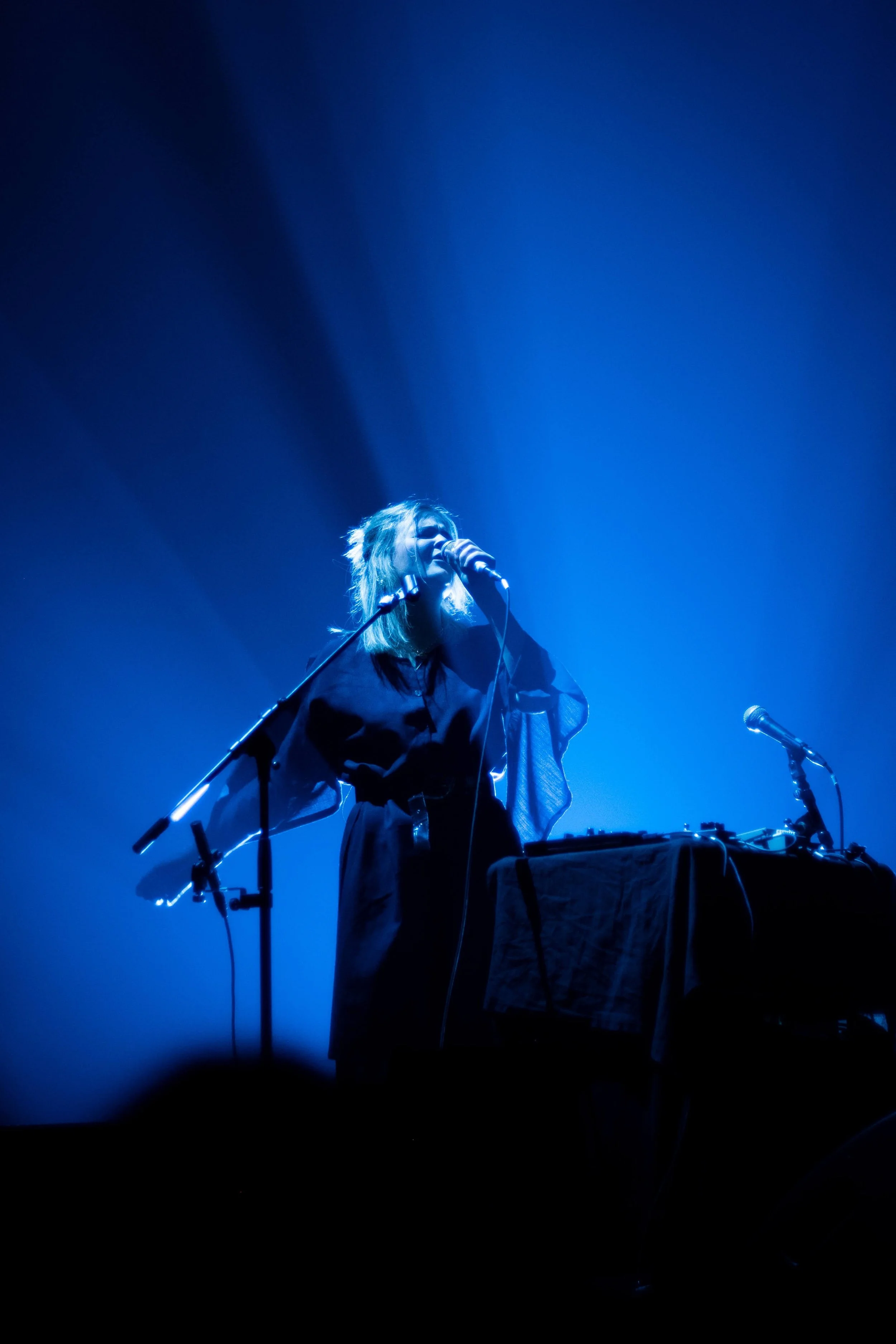 Photographe concert - Une femme chante ou joue dans un spectacle avec un éclairage bleu, derrière un clavier ou une console musicale.
