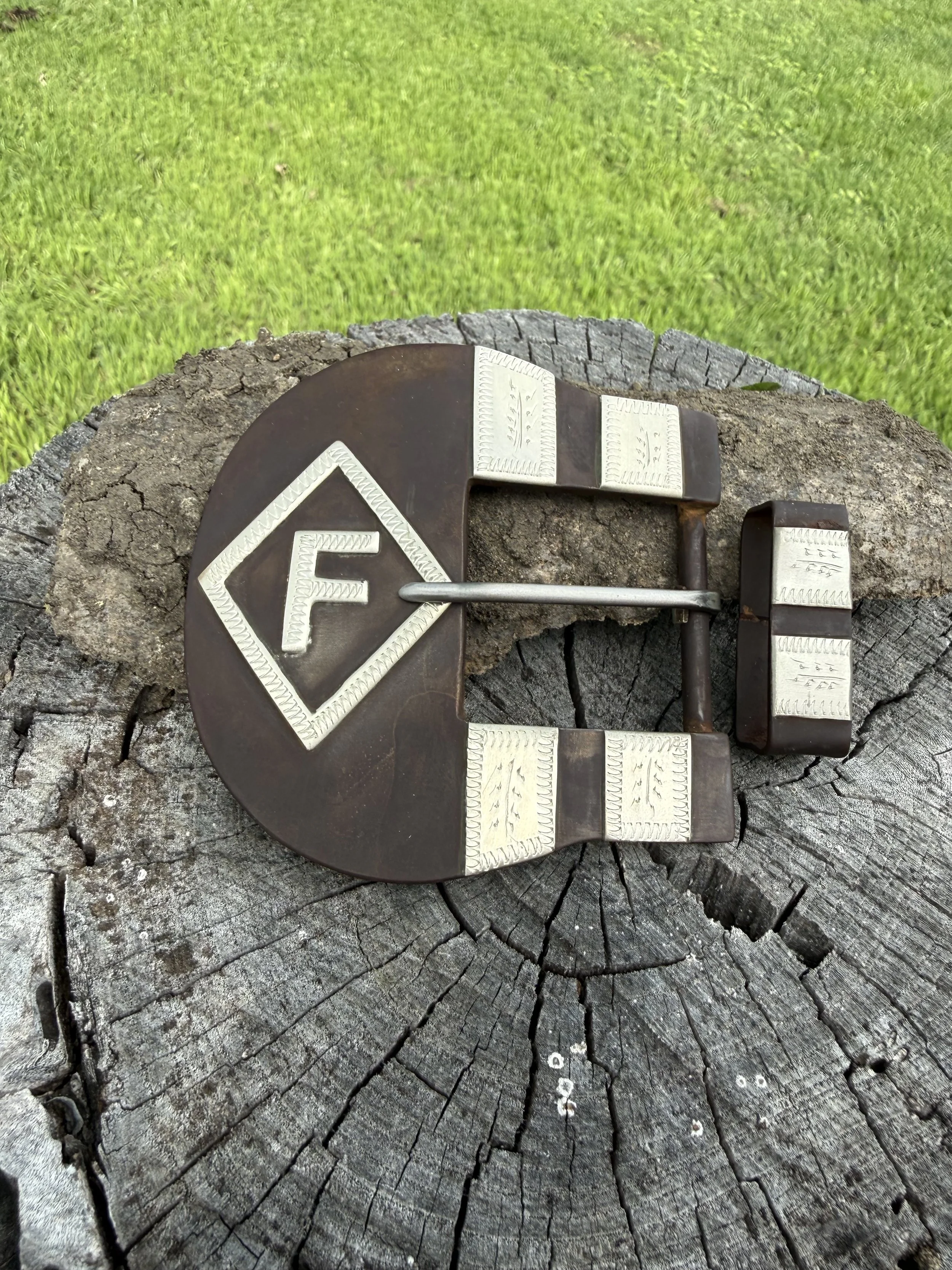 A handbag with a metal clasp lying on a tree stump with green grass in the background.
