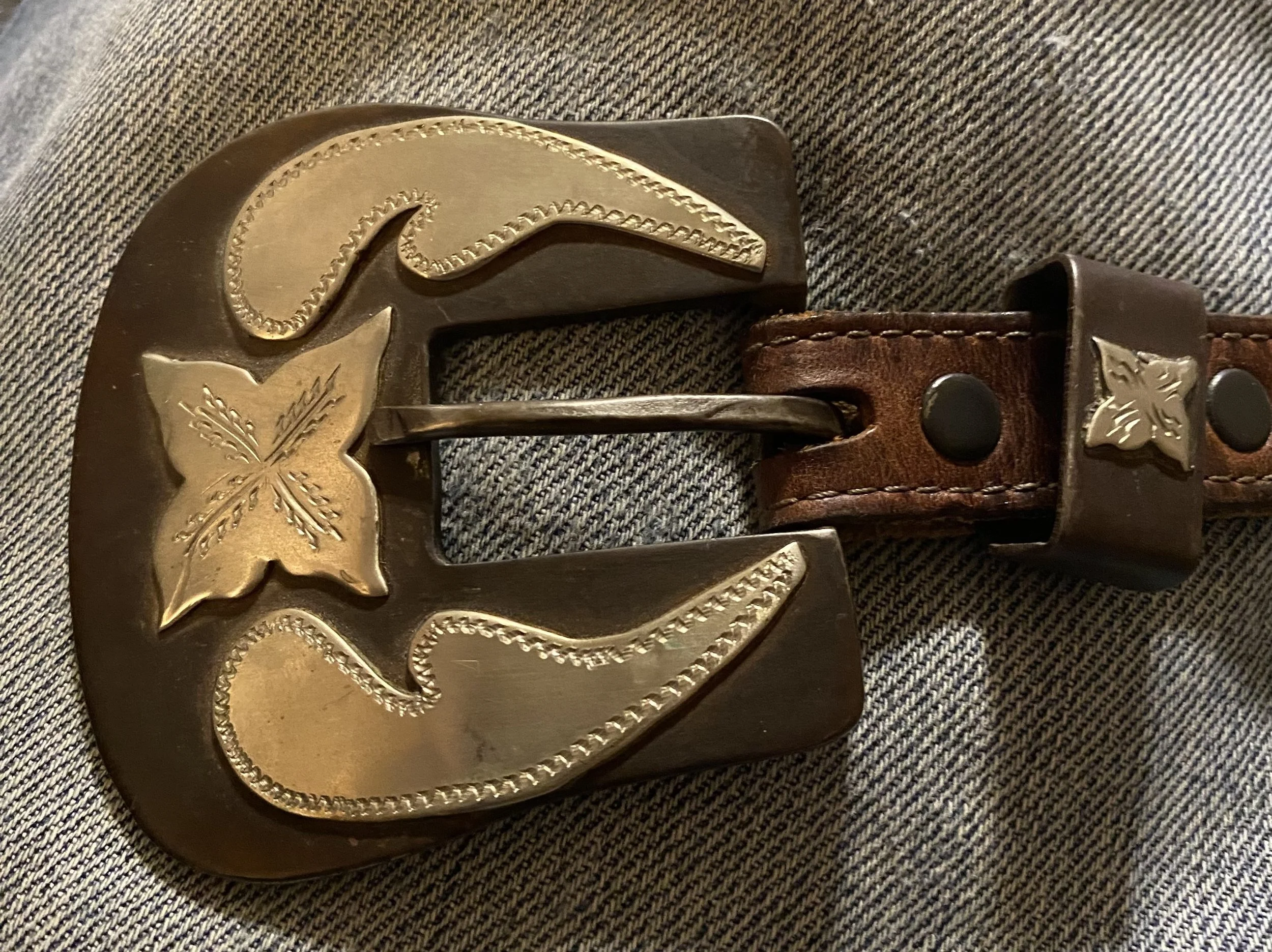 Close-up of a belt buckle with a gold and black design, featuring artistic patterns and embellishments, resting on fabric.