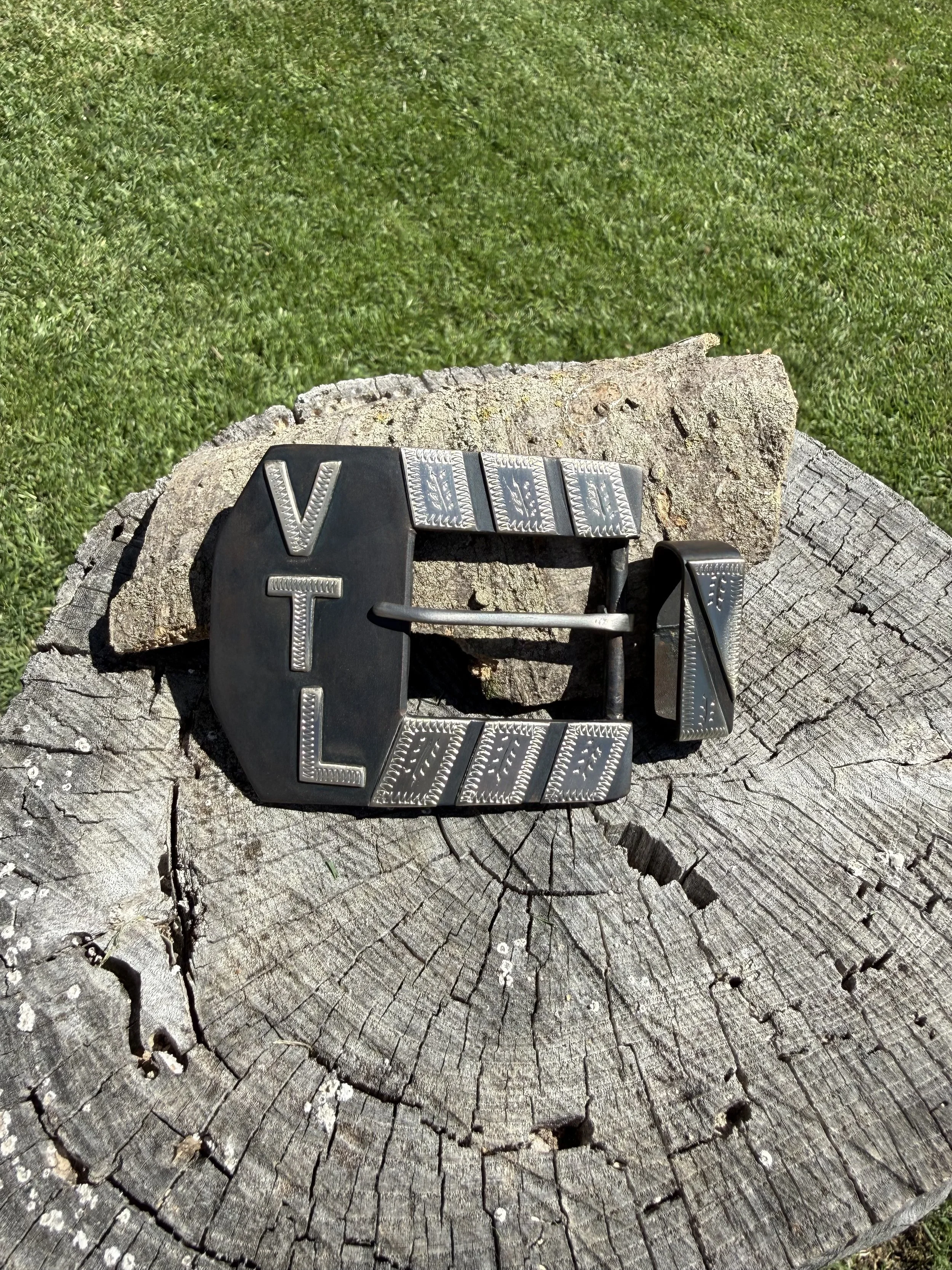 Close-up of a tree stump with a vintage belt buckle on top, garden grass in the background.