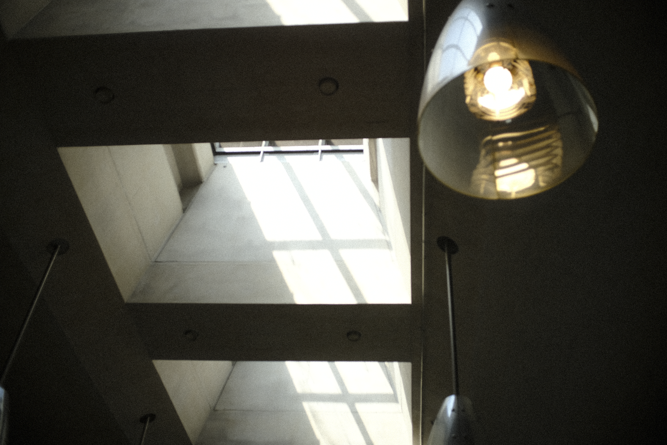 View of a skylight with sunlight streaming through a window, casting shadows on the floor, and a hanging metallic light fixture in the foreground.