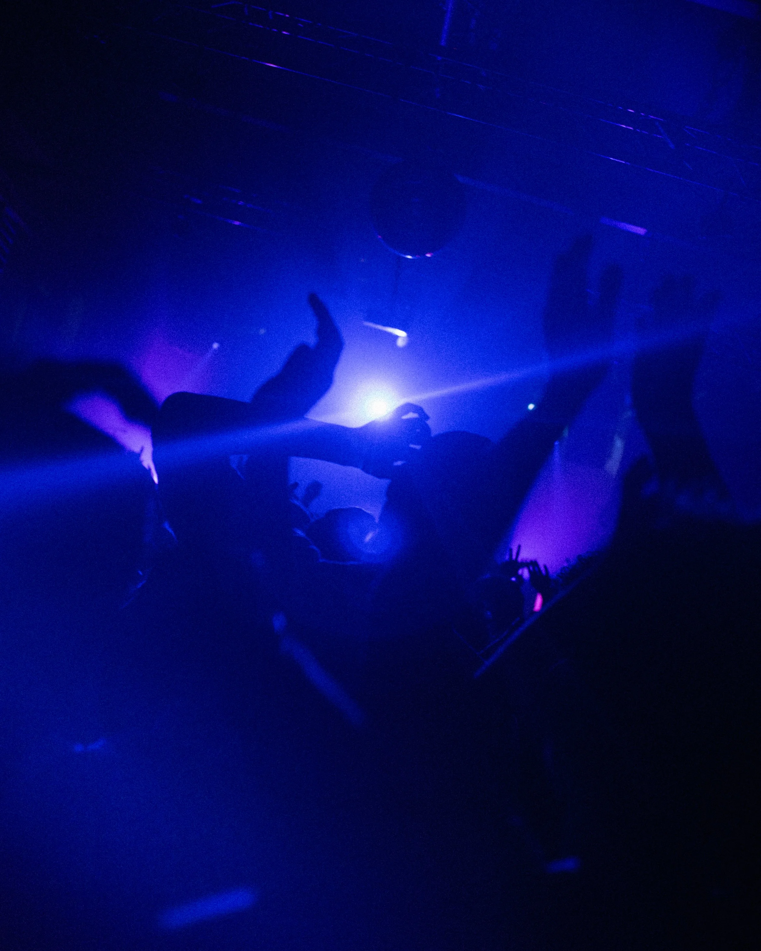 People dancing and enjoying themselves at a nightclub with purple and blue lighting and silhouetted figures.