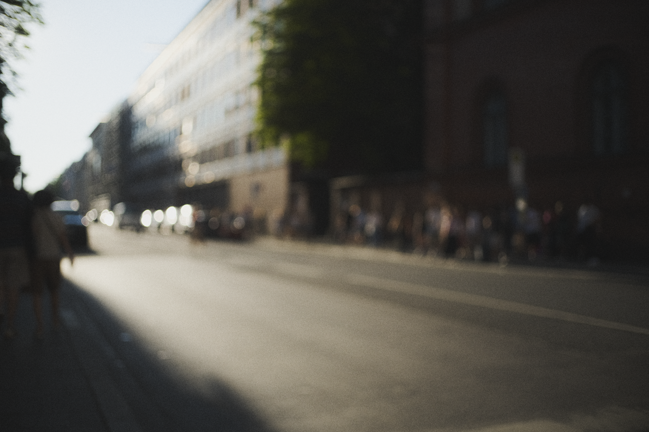 Blurred city street scene with people walking on the sidewalk and cars on the road, buildings on both sides.