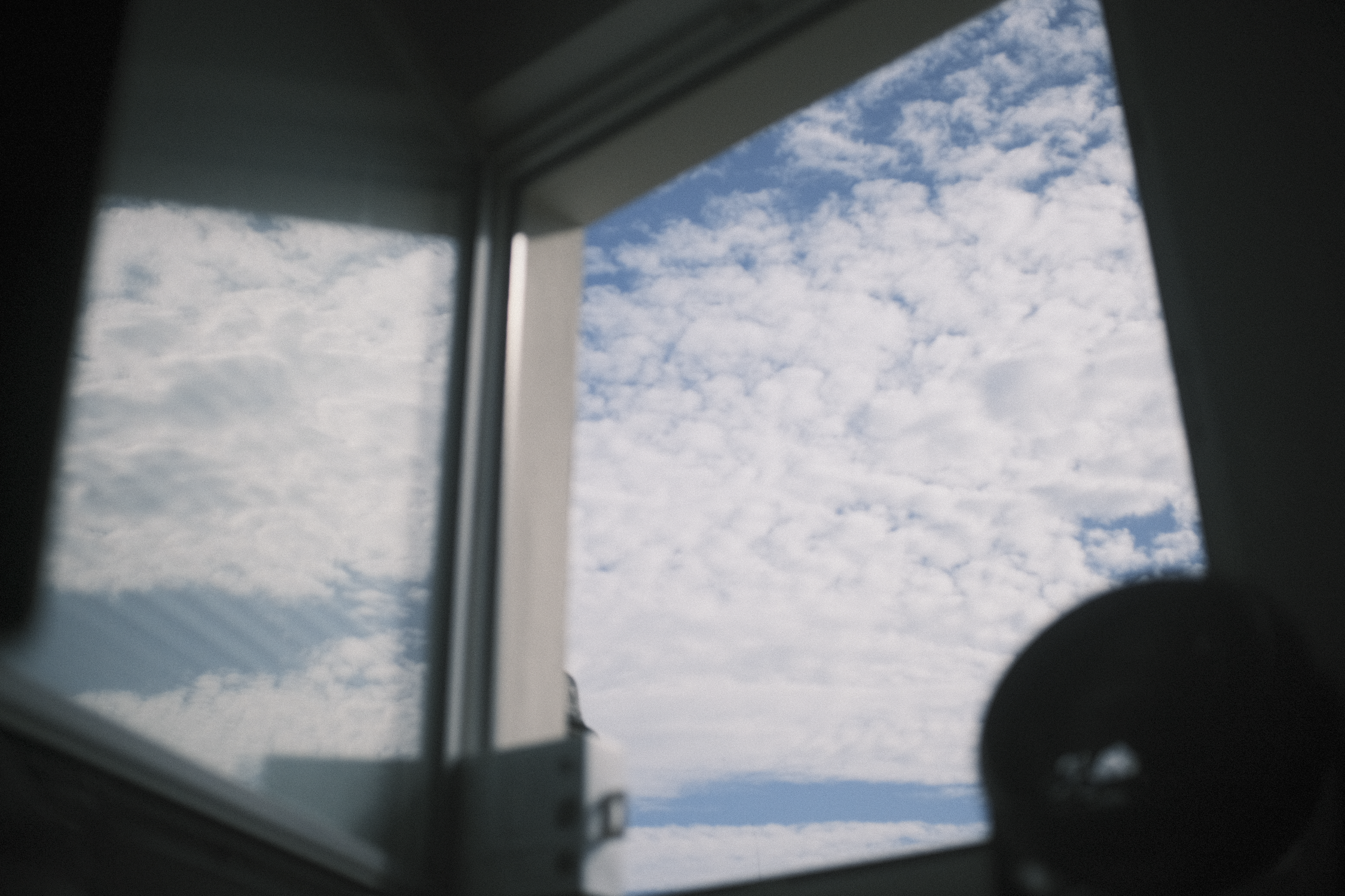 View through a window showing a blue sky with scattered clouds.