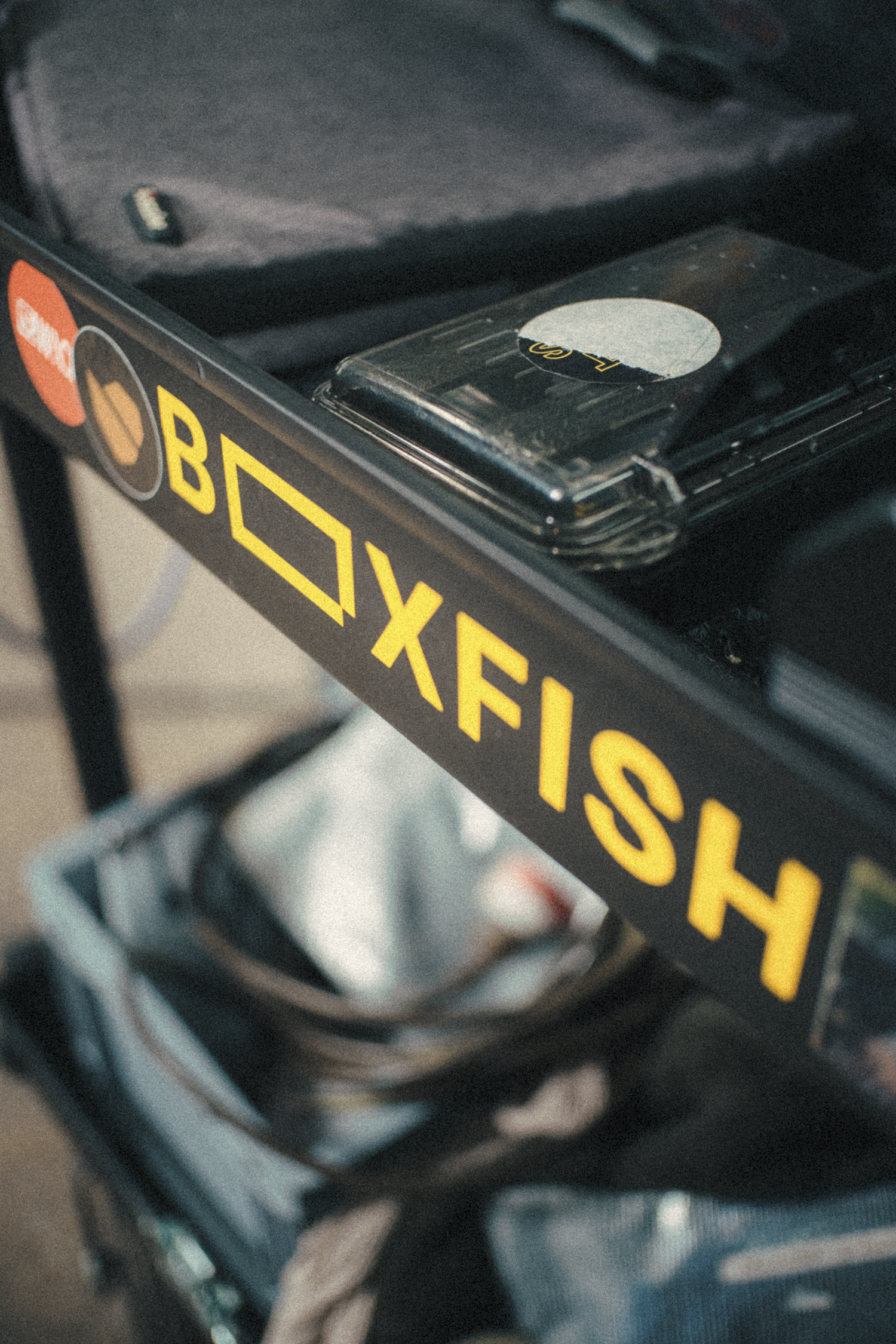 Close-up of a black box labeled 'BOXFISH' with yellow text and stickers, next to a smartphone inside a car or storage area.