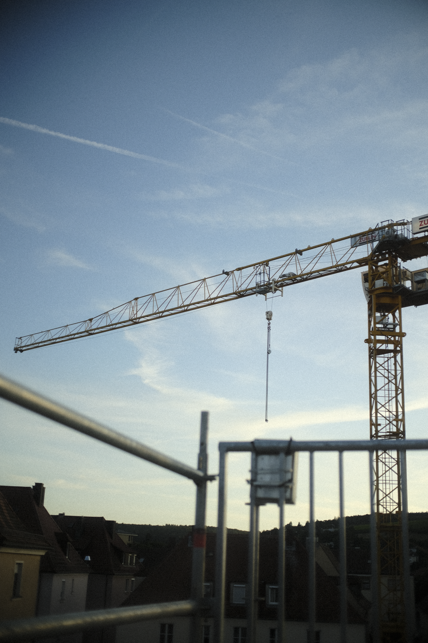 Construction crane on a building site under a blue sky with some clouds and contrails.