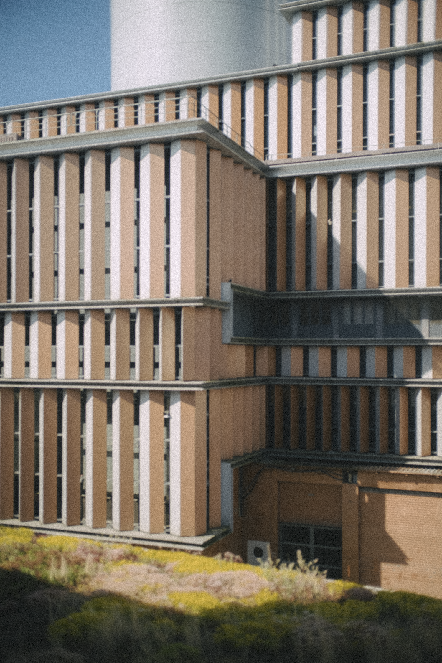 Close-up of a modern building with vertical beige and white panels, multiple levels, and shadows cast by the structure.