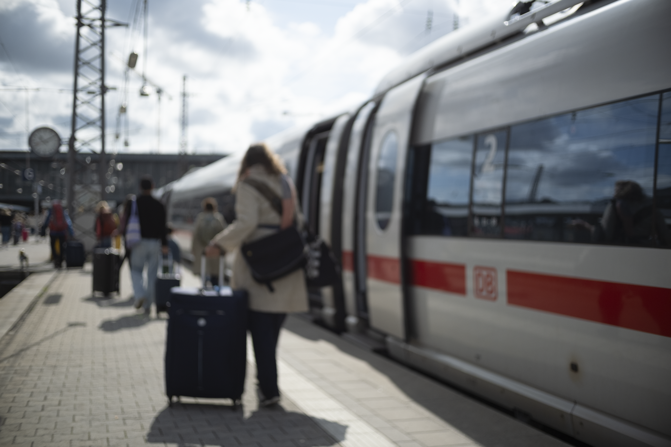 Blurred image of travelers boarding a high-speed train at a train station platform on a partly cloudy day.