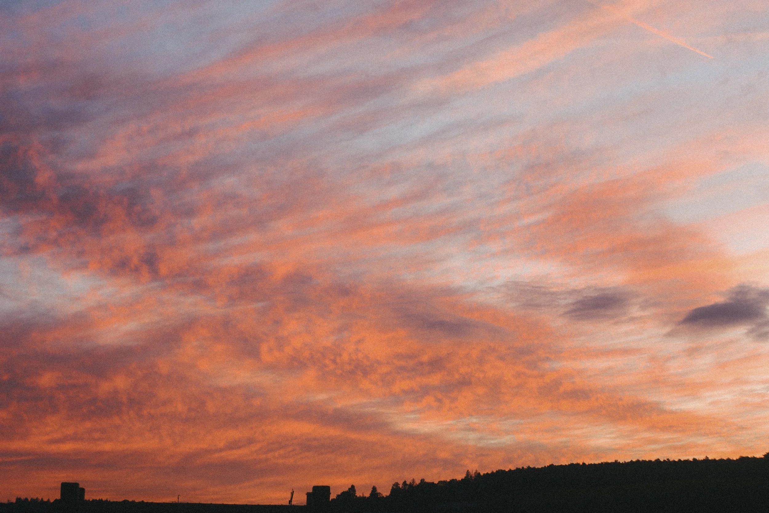 A colorful sunset sky with orange, pink, and purple hues over a silhouetted landscape with trees and buildings.