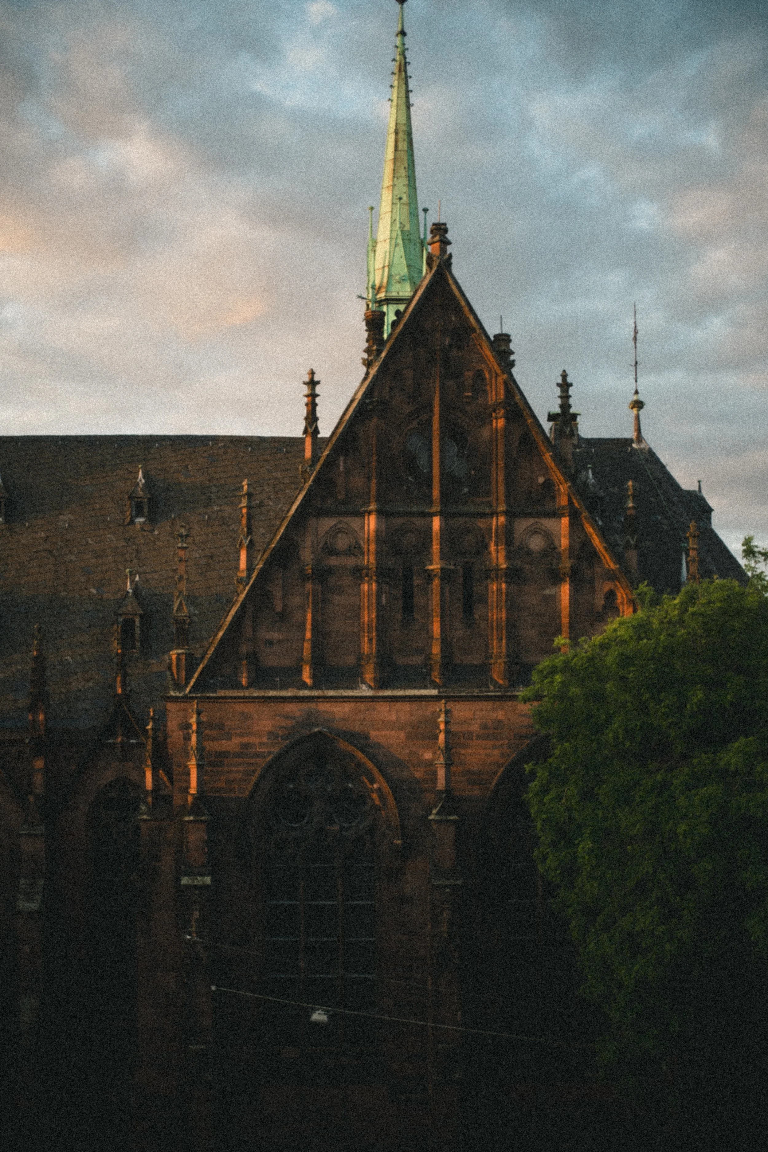 A Gothic-style church with a tall, pointed spire, characterized by large arched windows and ornate architectural details, set against a cloudy sky at dusk.