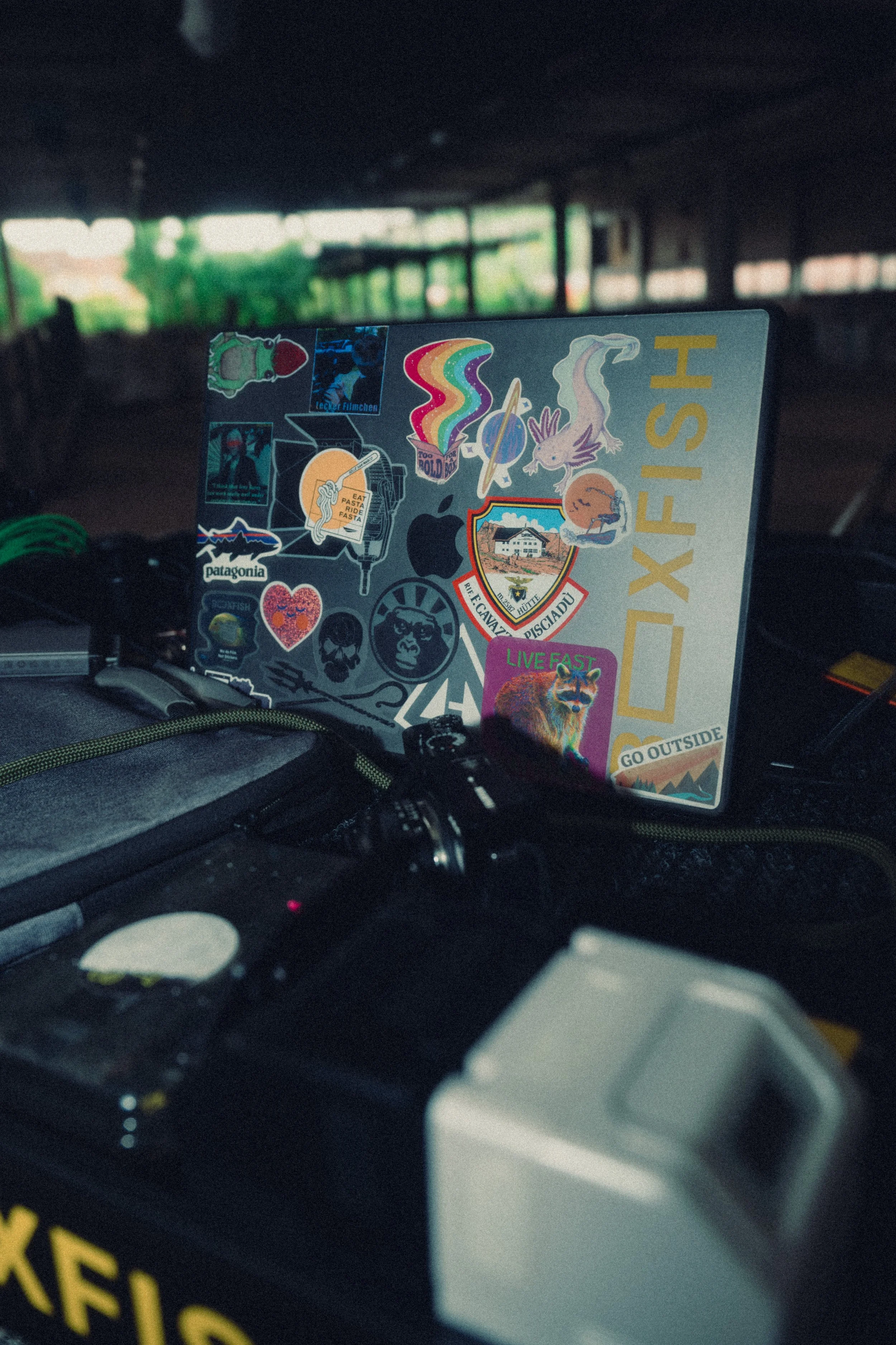 A laptop covered in colorful stickers, placed on a vehicle dashboard, with a blurred background of a tunnel or underpass and greenery outside.
