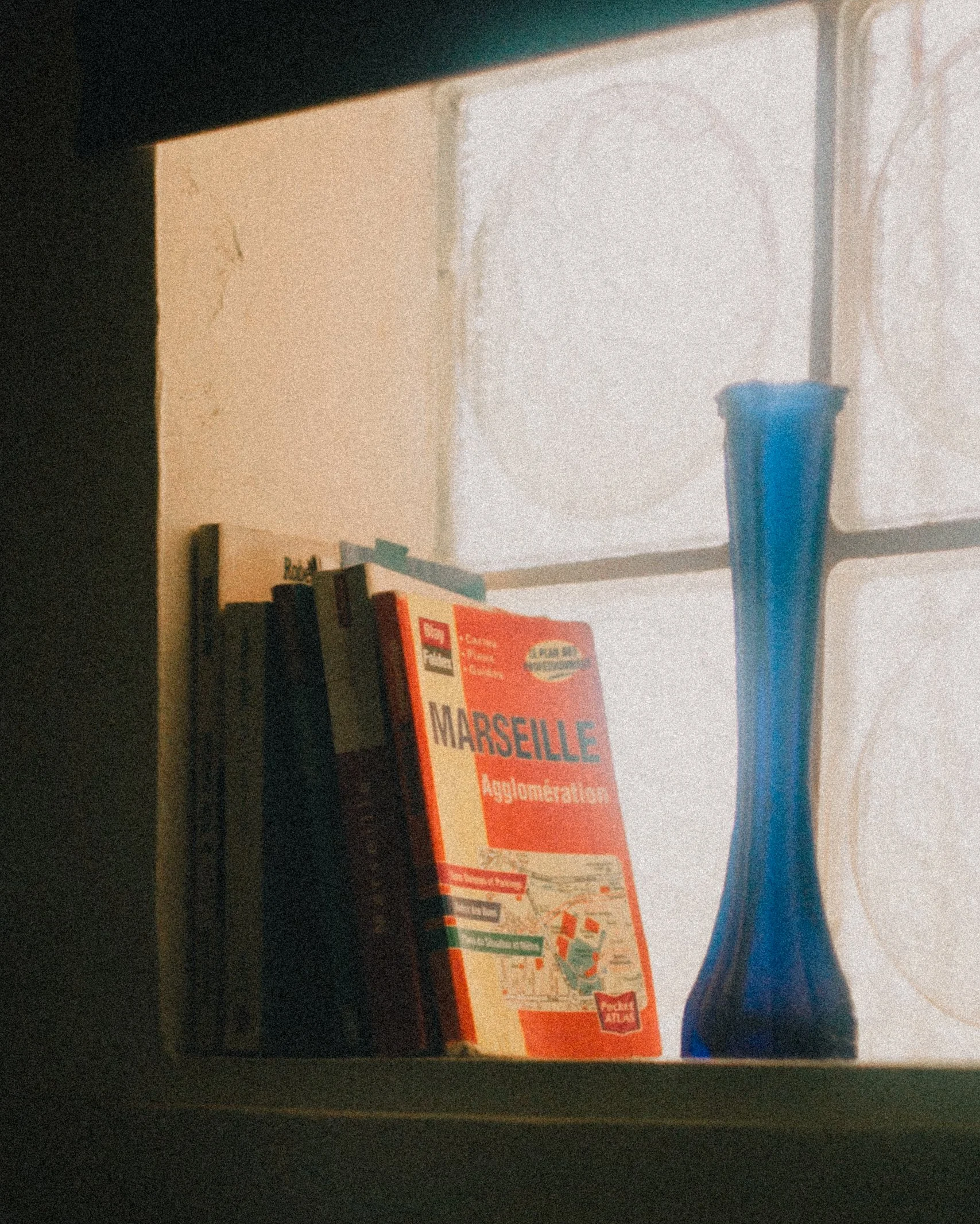 A bookshelf with books and a blue glass vase placed near a window with frosted glass.