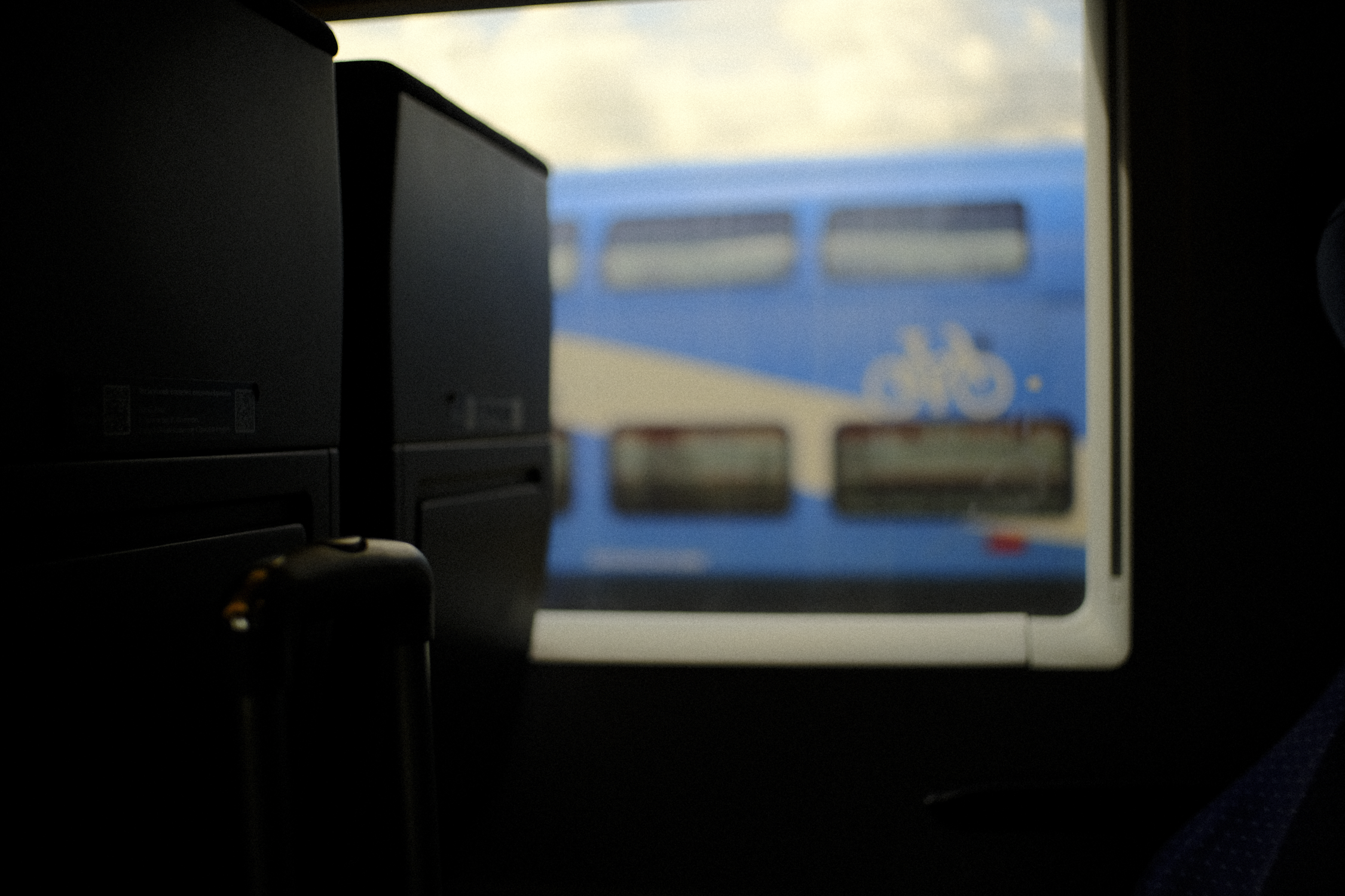 Inside an airplane, view through the laptop screen showing a blue train with a bicycle symbol on it outside the window.