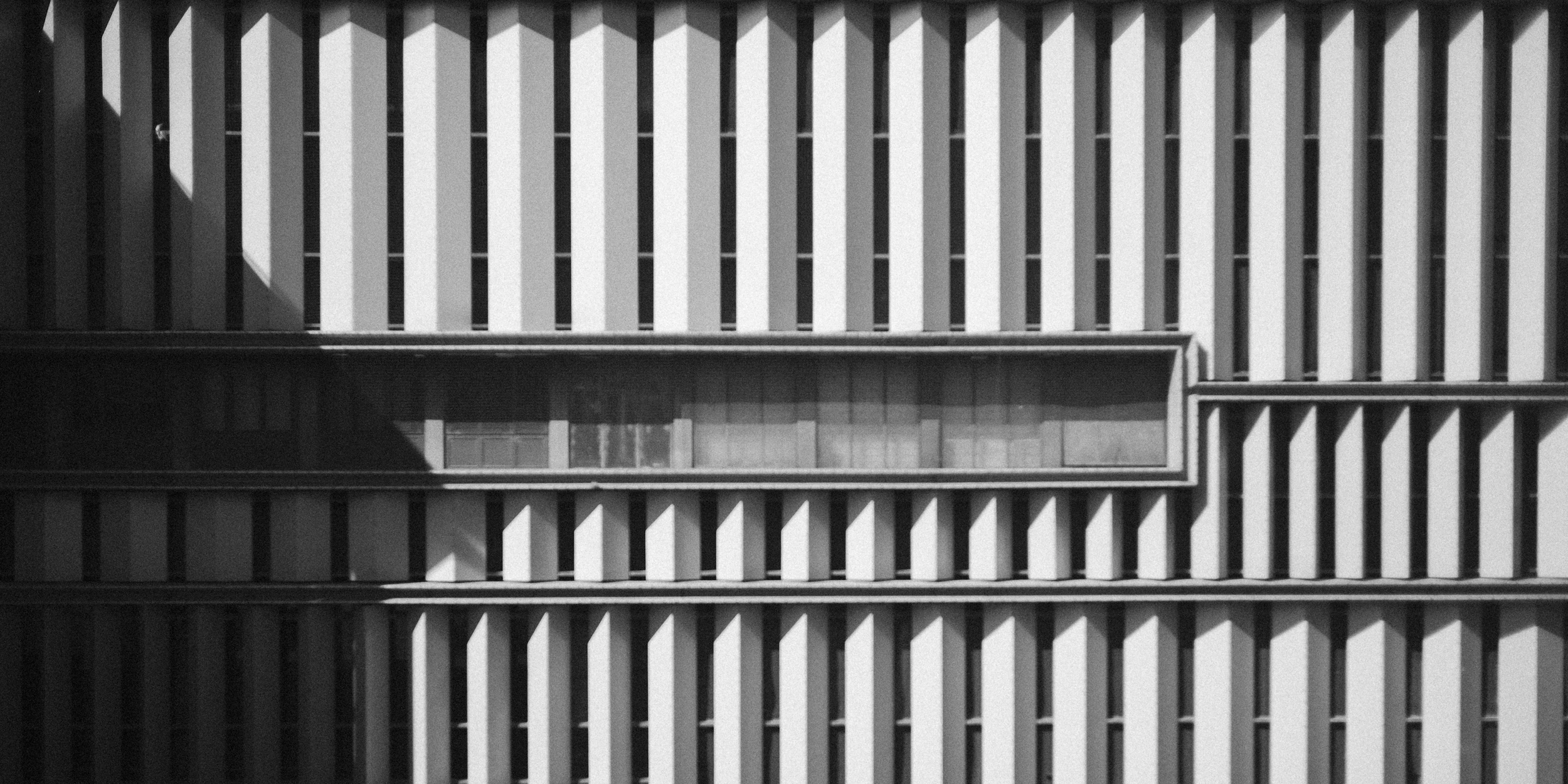 Close-up of a modern building's exterior, featuring a pattern of vertical white and dark panels with a horizontal section of windows.