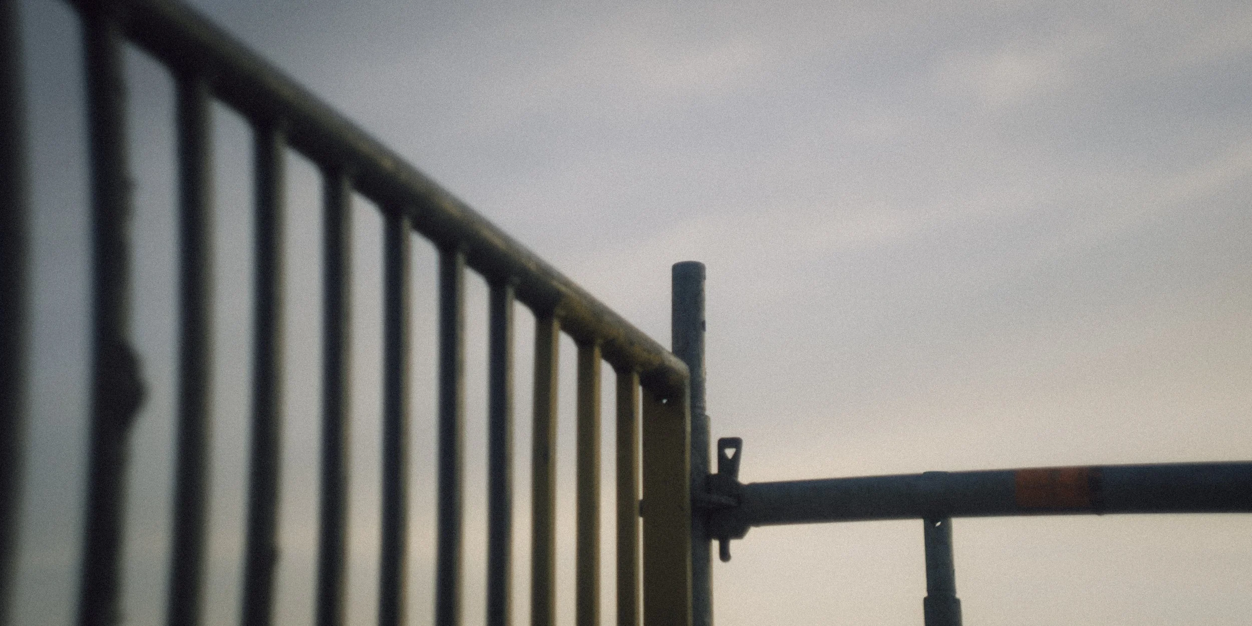 Close-up of a metal fence with vertical bars and a background of cloudy sky.