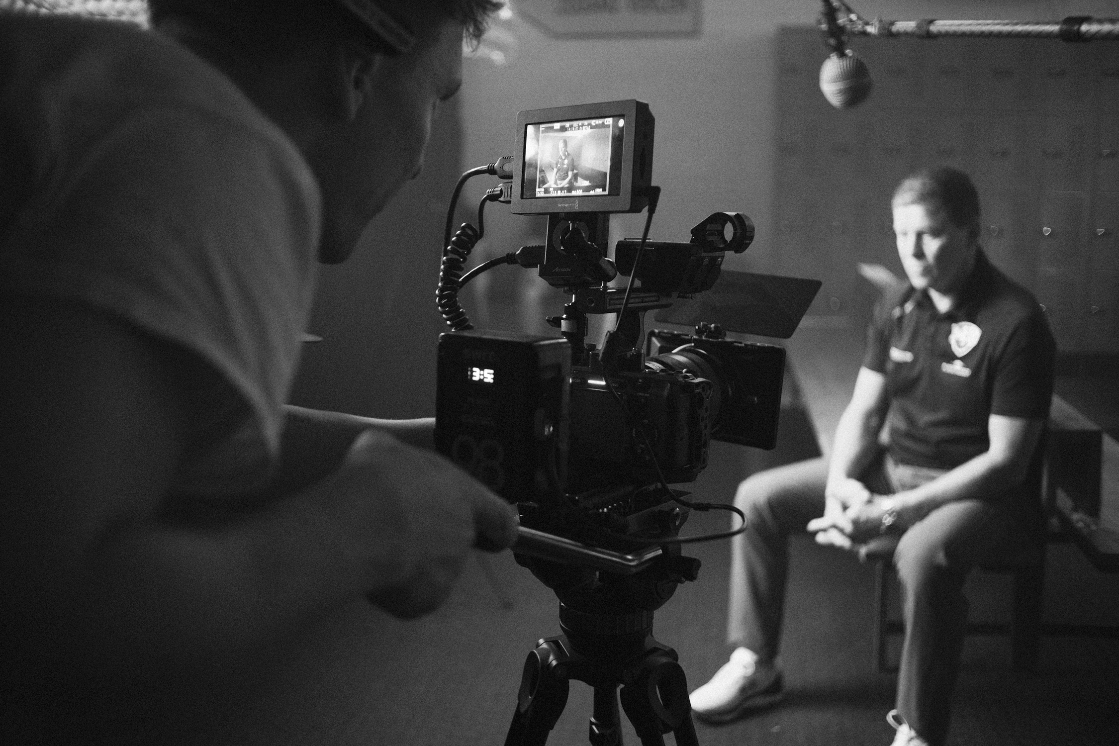 Black and white photo of a man operating a professional camera filming a man in a police uniform for a video or interview inside a studio.
