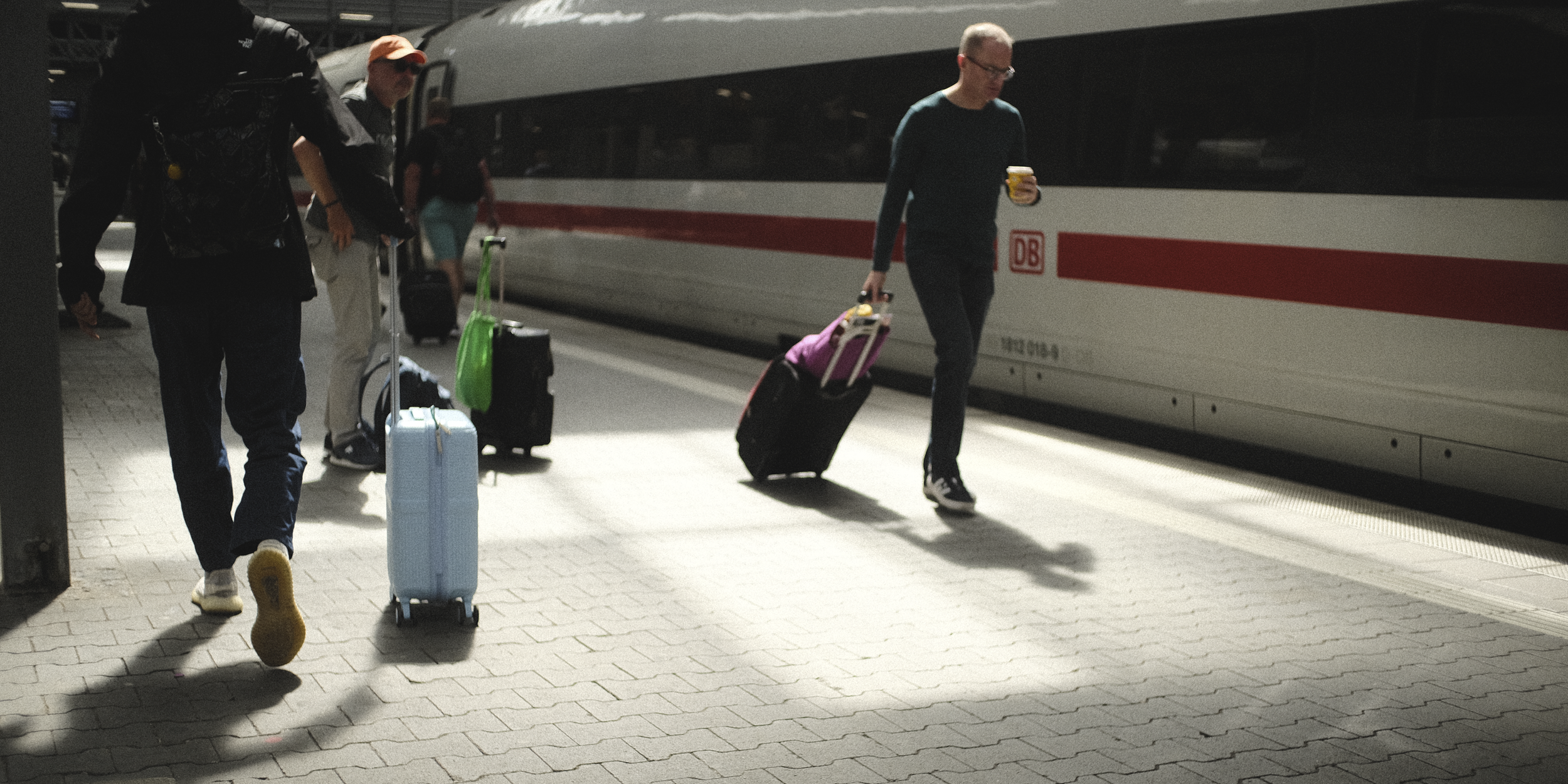 People walking with rolling suitcases on a train platform next to a Deutsche Bahn train.