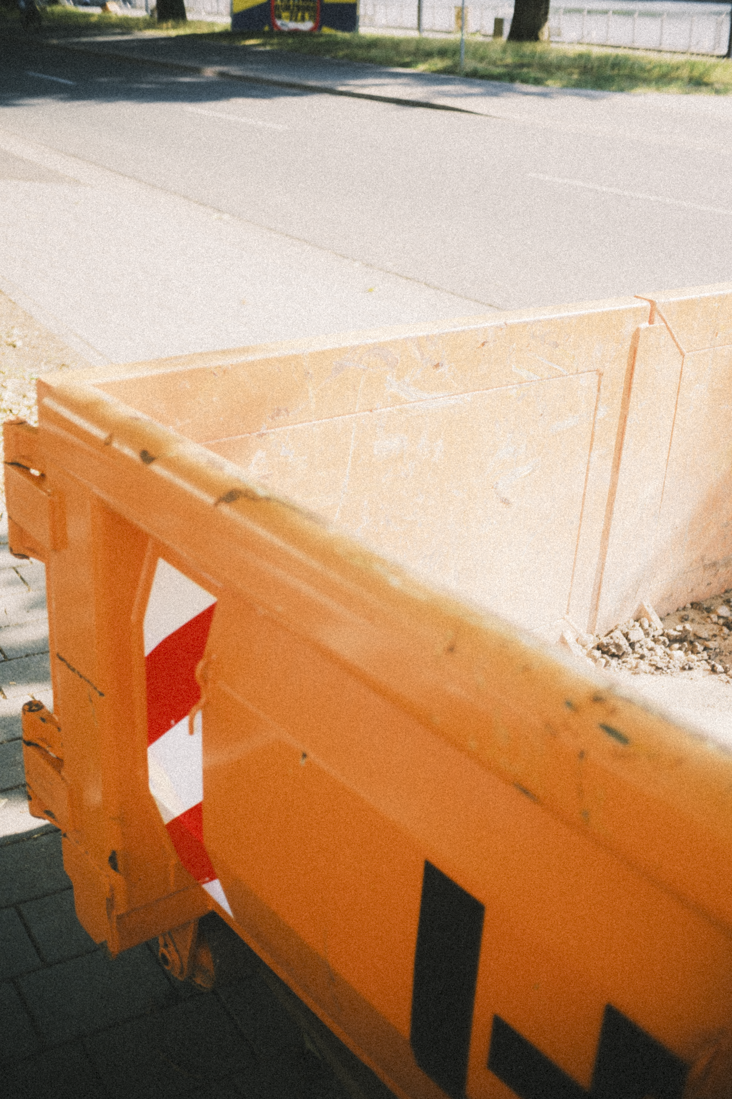 Orange construction barrier on sidewalk with a street and bus stop in the background.