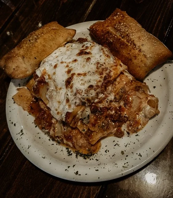 Plate of lasagna with two breadsticks, garnished with herbs.