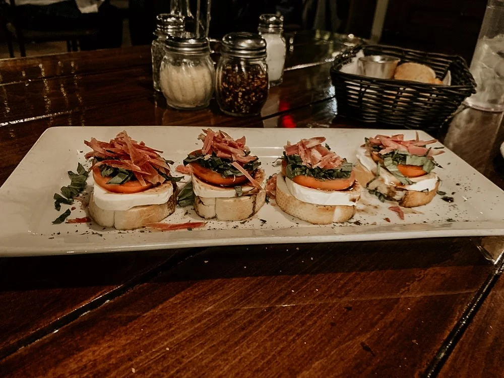 Four pieces of open-faced sandwiches with tomato, greens, cheese, and shredded meat on a white platter.