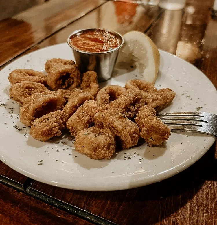 Fried calamari served on a white plate with a lemon wedge, a small cup of marinara sauce, and a fork.
