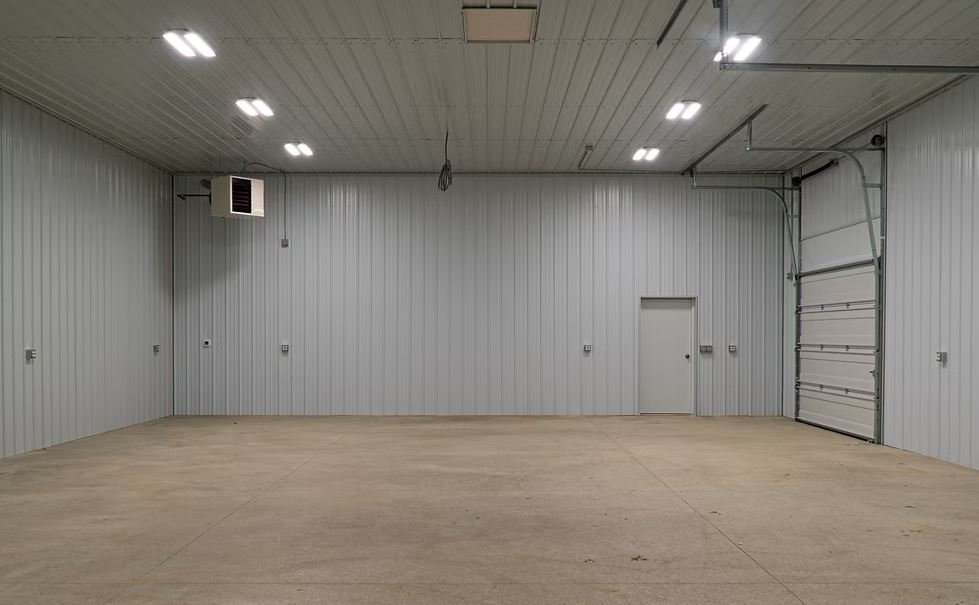 Empty clean garage with metal walls, ceiling lights, a small door, and a large garage door.