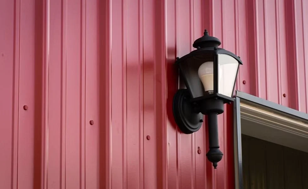 Black outdoor wall-mounted lantern on a red metal building exterior.