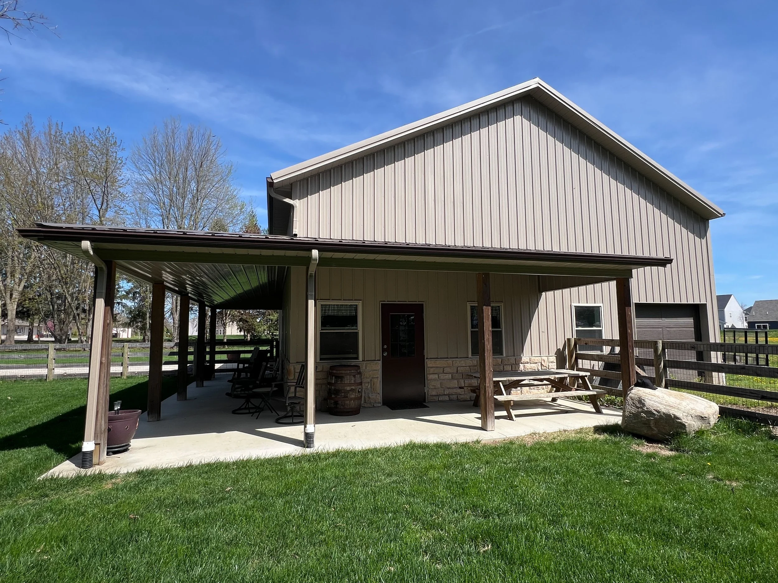 Backyard view of a house with a covered patio, green grass, trees, and a clear blue sky.