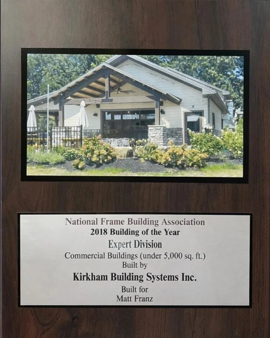 Photo of a modern house with a large covered porch, surrounded by greenery and flowering bushes, awarded by the National Frame Building Association in 2018.