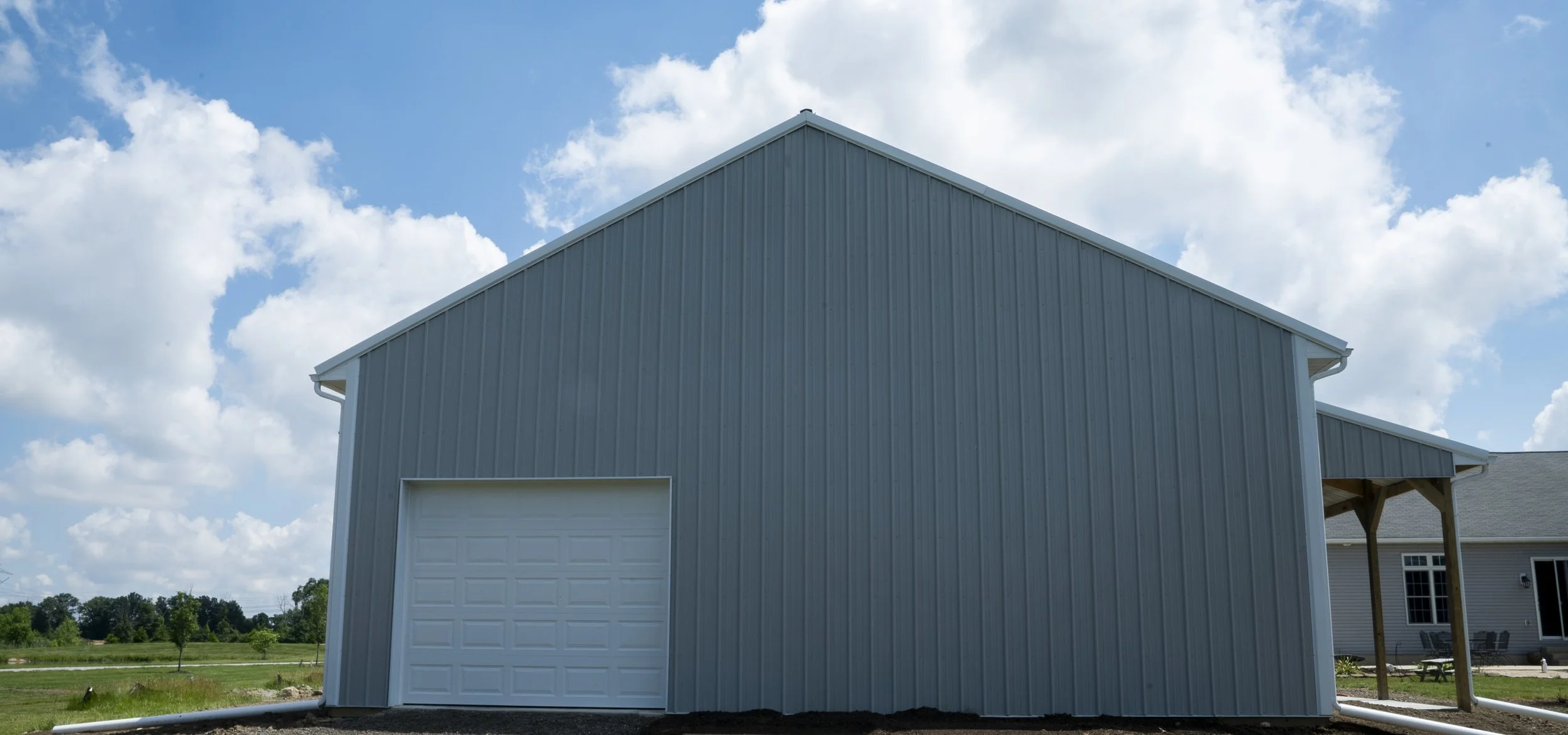 A light blue garage with a closed white garage door, situated under a partly cloudy sky in a rural setting.
