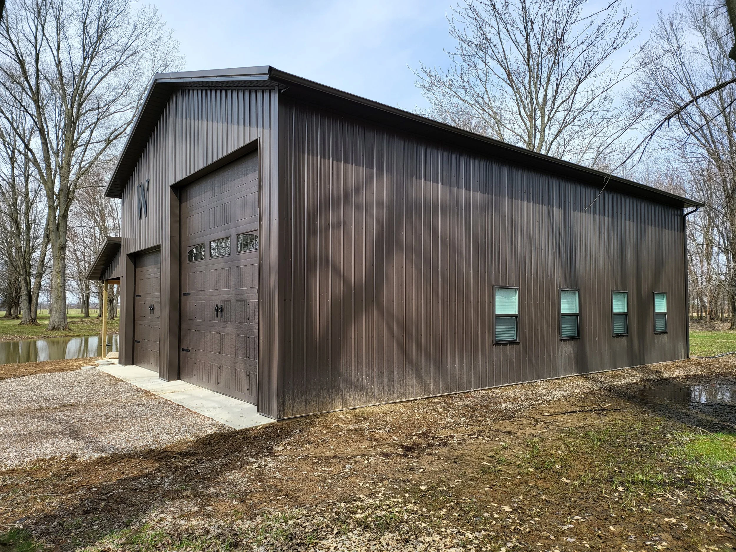 Metal building with large garage doors in a wooded area during daytime.