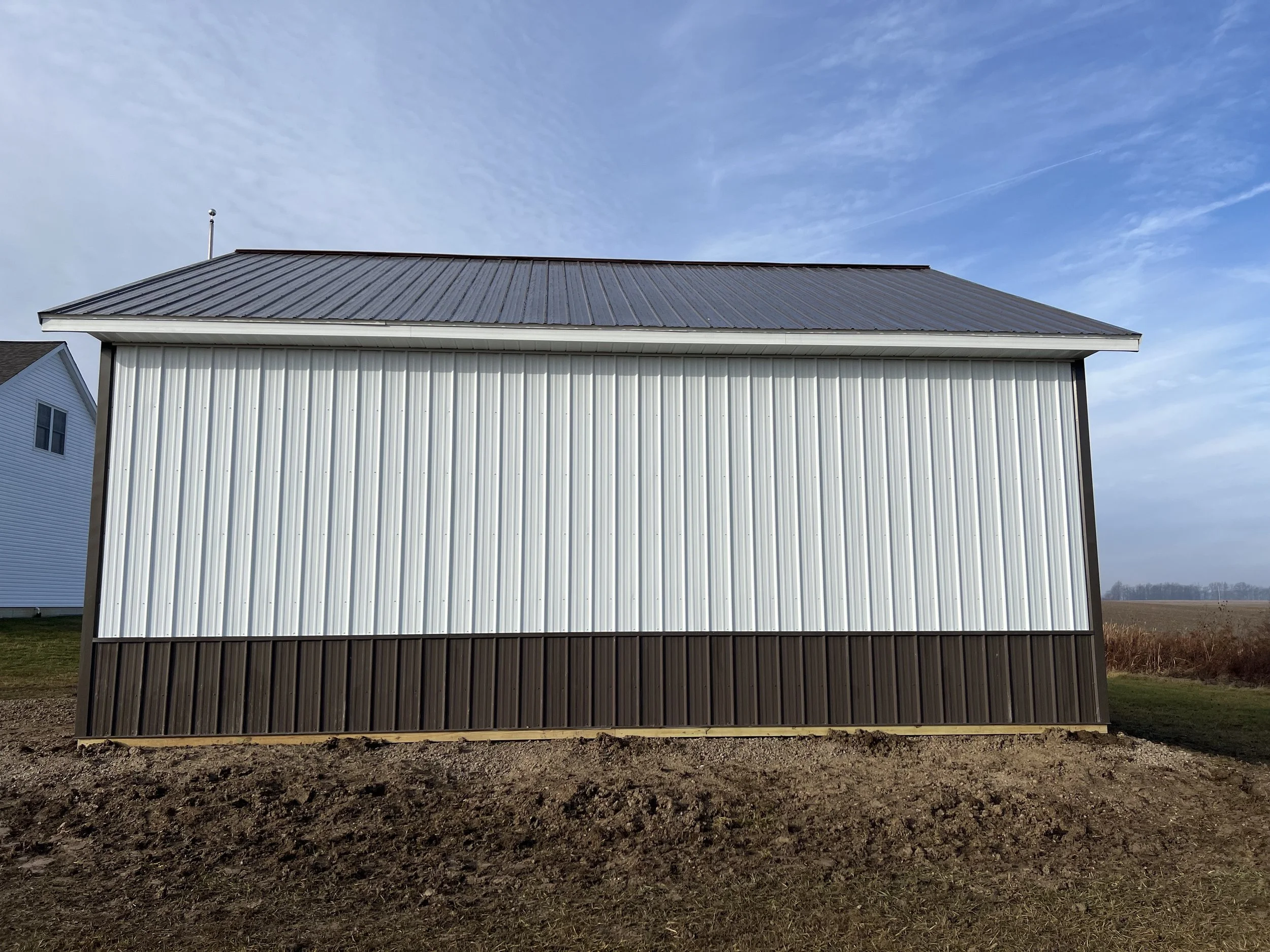A large barn with a metal roof and metal siding in an open field with a partly cloudy sky.