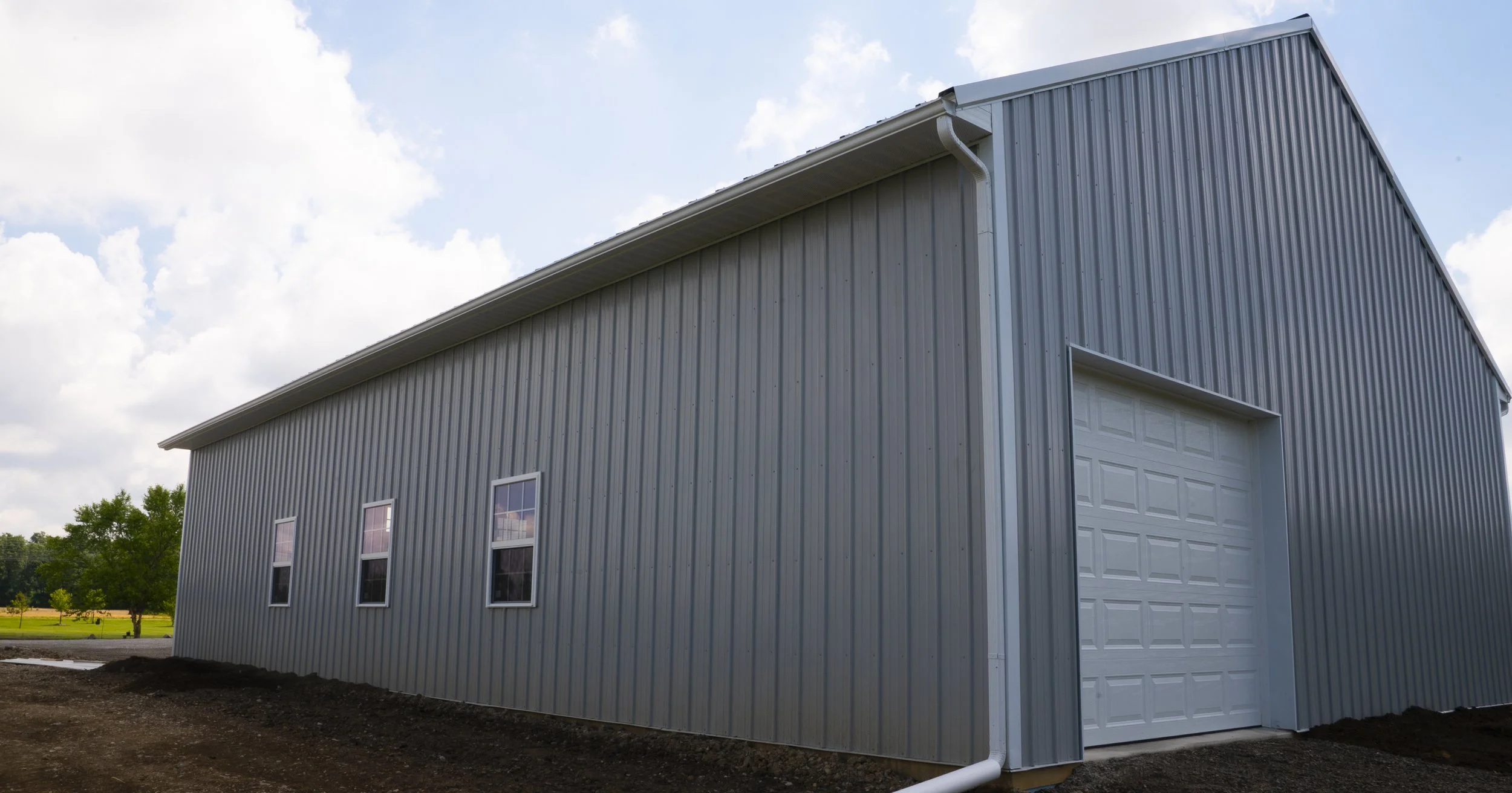 A large blue metal building with a white garage door and four windows on the side, set against a partly cloudy sky.