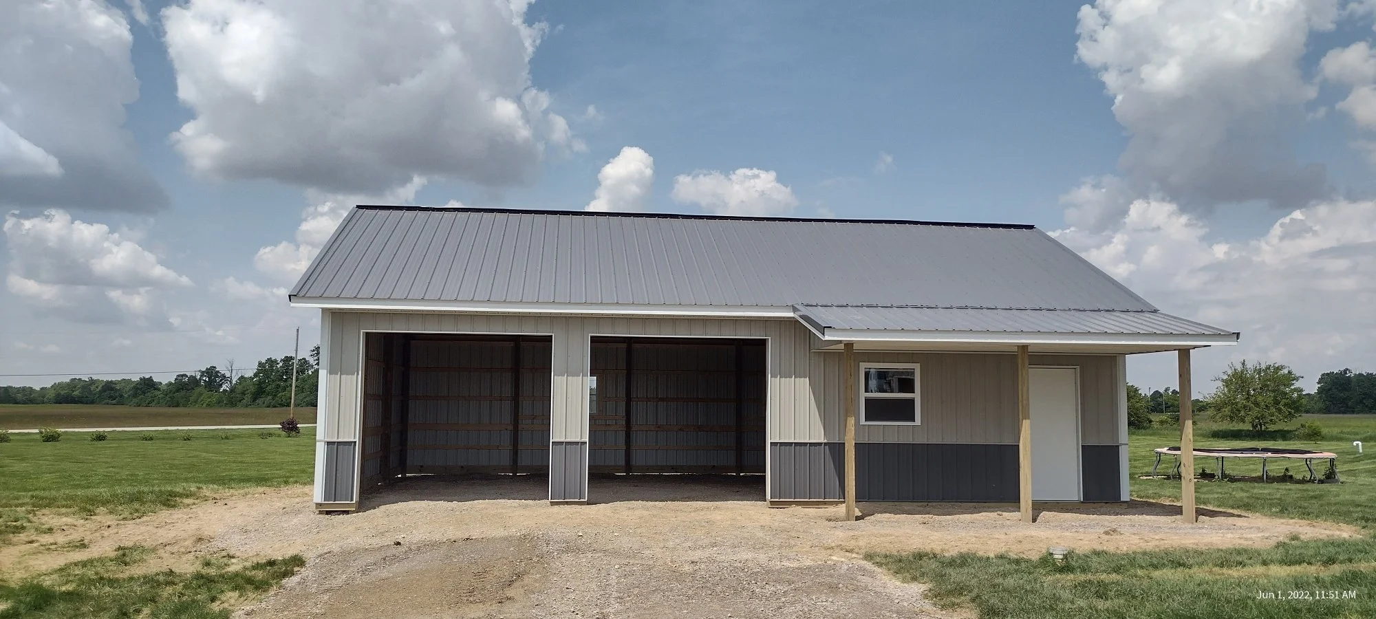 A metal building with a gray roof and white and gray siding, set on a grassy field under a partly cloudy sky.