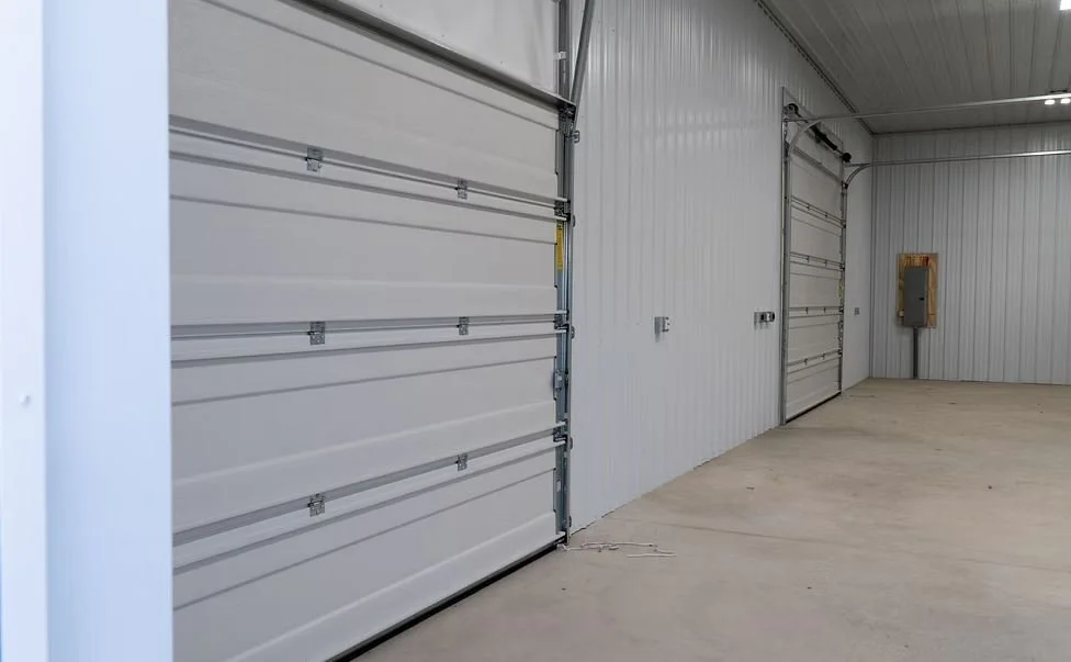 Interior of a warehouse or garage with two large metal garage doors and an electrical panel on the wall.