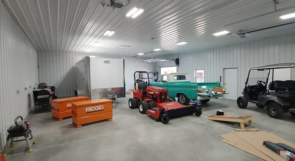 A spacious garage with a variety of vehicles and equipment, including a red lawn mower, a vintage teal truck, a golf cart, and storage containers.