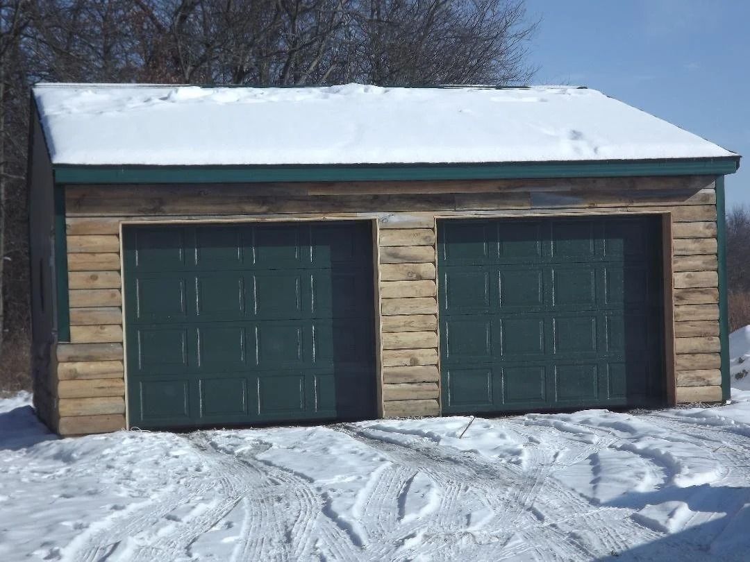 A wooden double garage with snow-covered roof and snow on ground in winter.