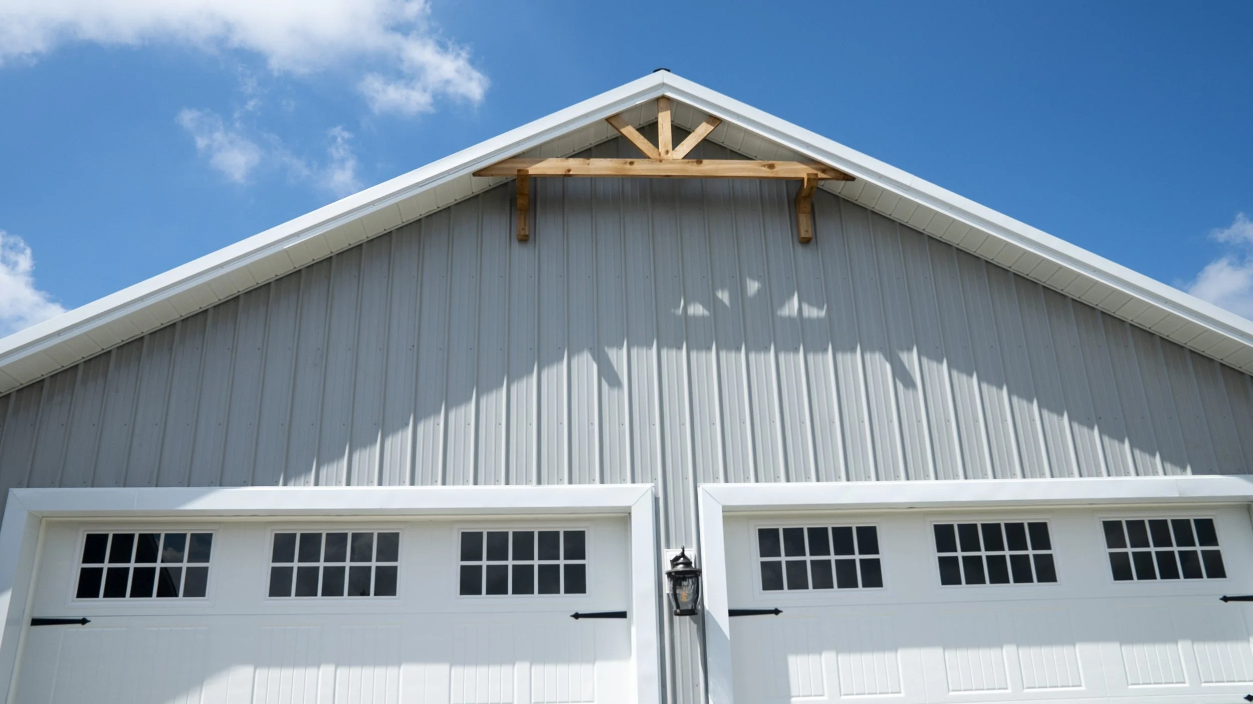 Front view of a white barn with metal siding, decorative windows, and a sliding door, under a blue sky with some clouds.