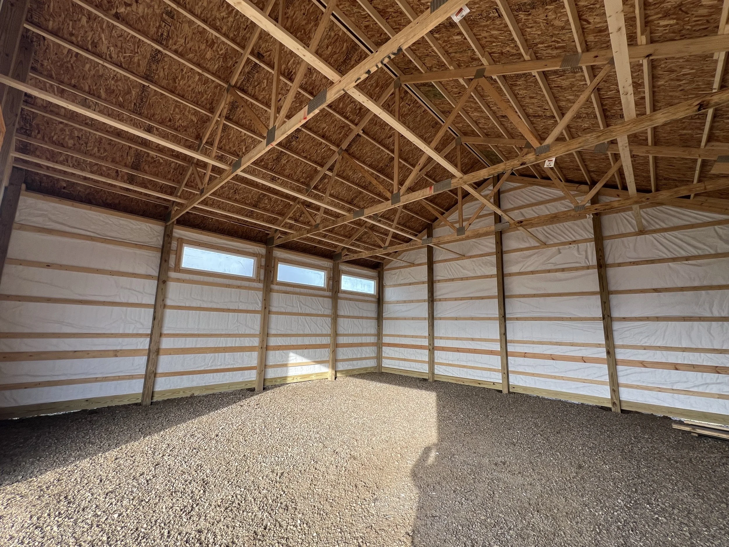 Interior of a building under construction with exposed wooden framing, insulation, roof trusses, and windows.