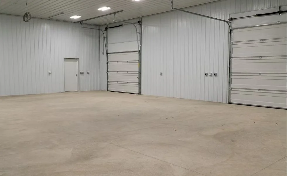 Empty indoor garage with white metal walls and two large roll-up doors.