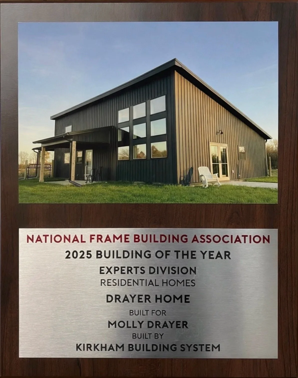 Plaque recognizing a building, a modern black metal home with large windows and outdoor seating, awarded as the 2025 Building of the Year by the National Frame Building Association in the Experts Division, built by Kirkham Building System for Molly Drayer.