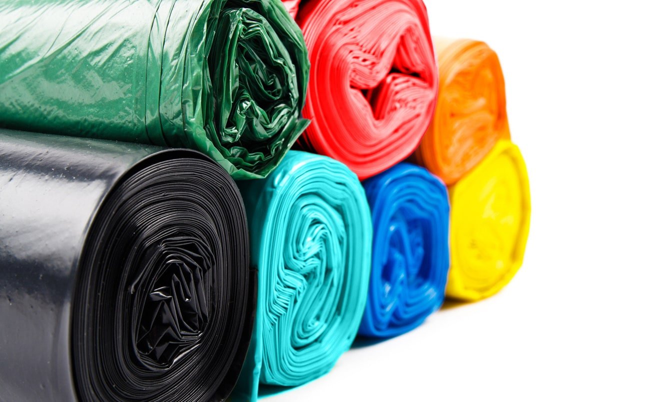 Rolled colorful plastic trash bags in black, blue, yellow, orange, red, and green.