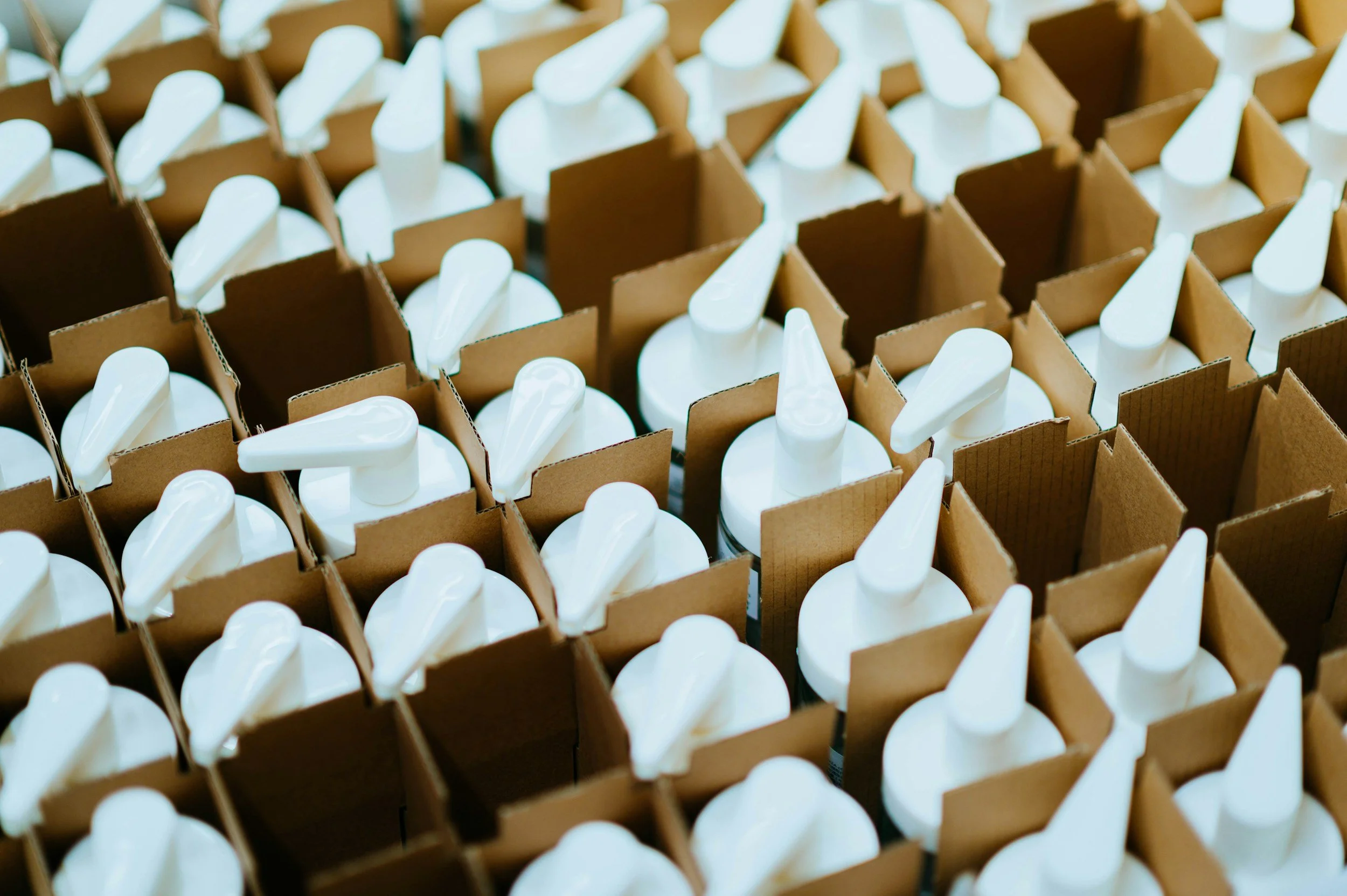 Rows of white plastic bottles with white pump dispensers stored in brown cardboard boxes.