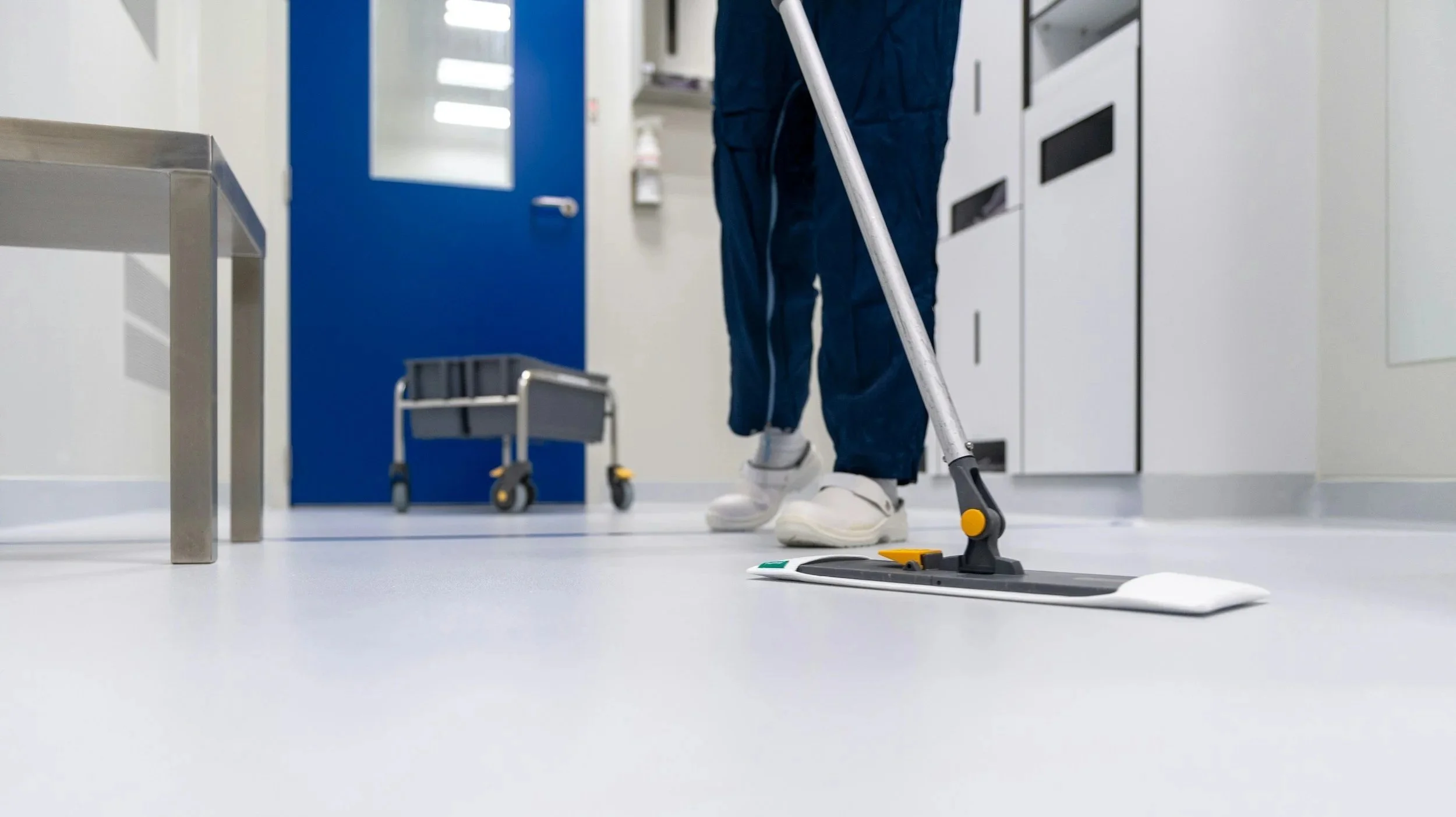 Person in blue scrubs using a robotic surgical device on a white floor in a hospital or medical facility.