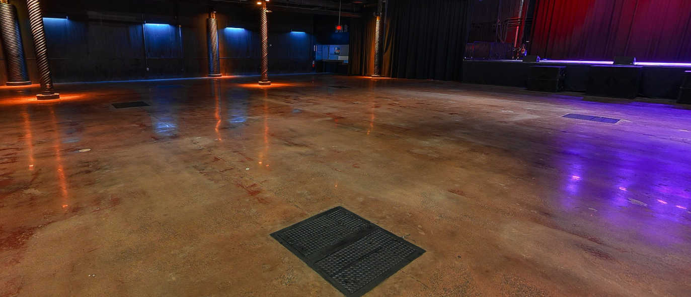 Empty dance floor with wooden flooring, illuminated by colorful stage lighting in a concert venue or nightclub.