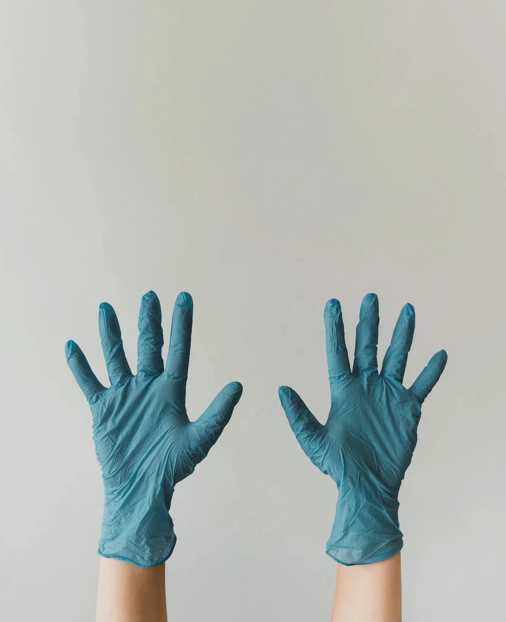 Two hands wearing blue medical gloves are reaching upward against a neutral background.