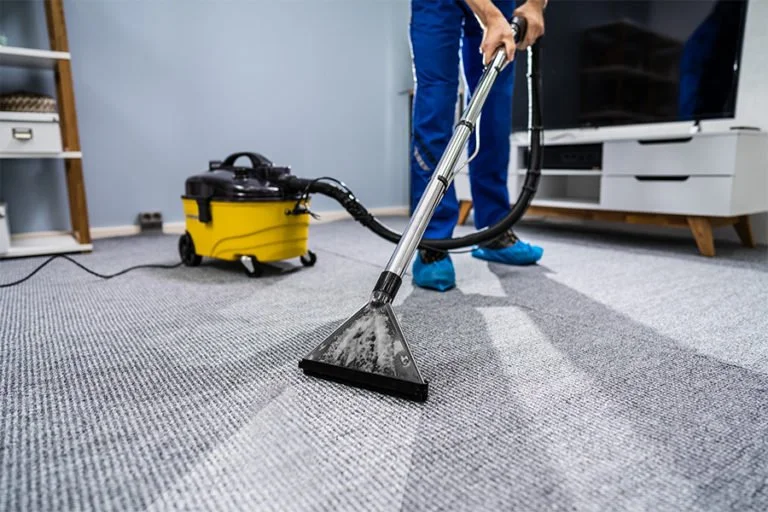 Person using a carpet cleaning machine to clean a gray carpet in a living room.
