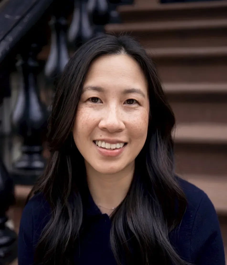 A woman with long dark hair smiling outdoors with a staircase.