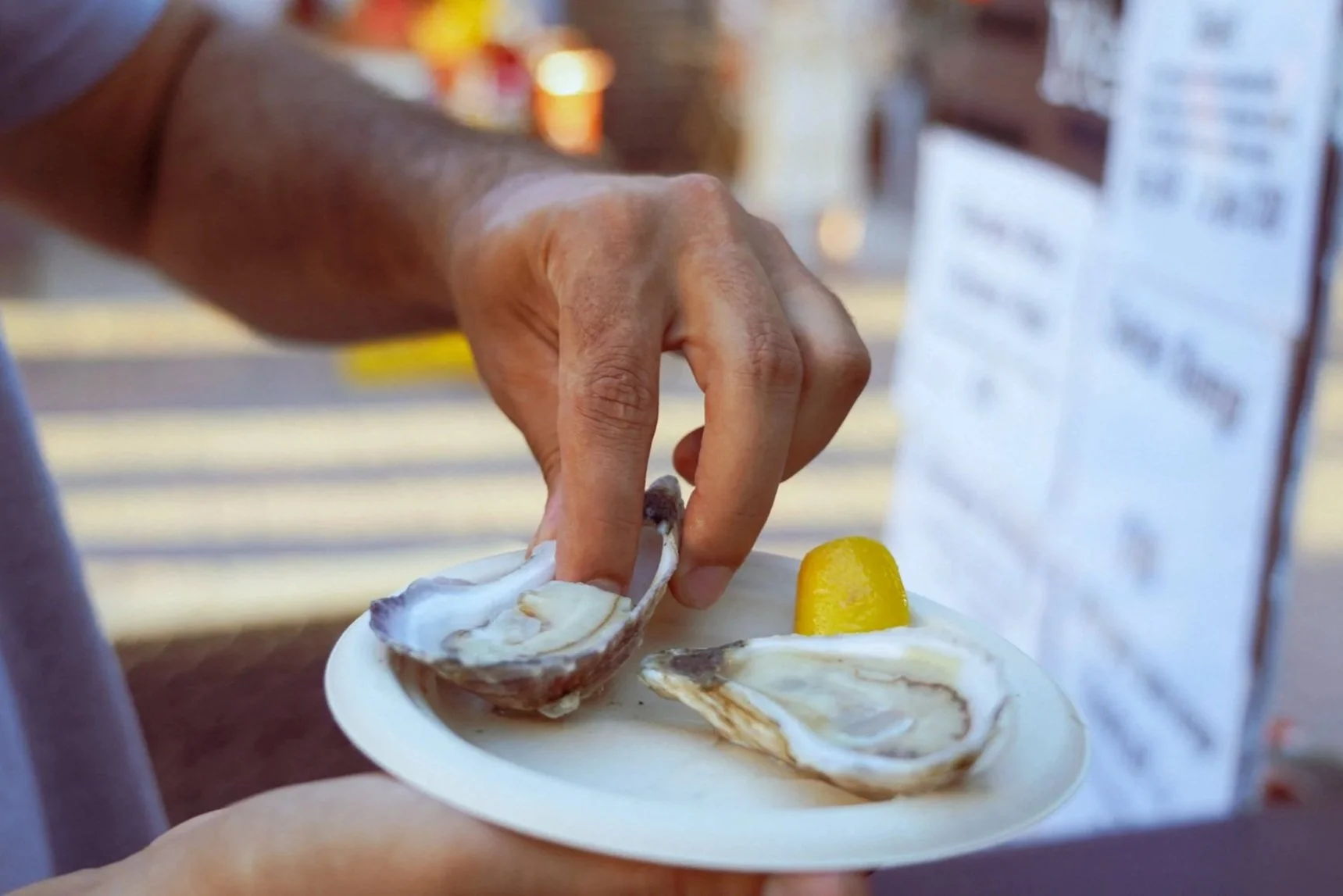 A person holding a plate with oysters and a lemon wedge, with a blurred background.