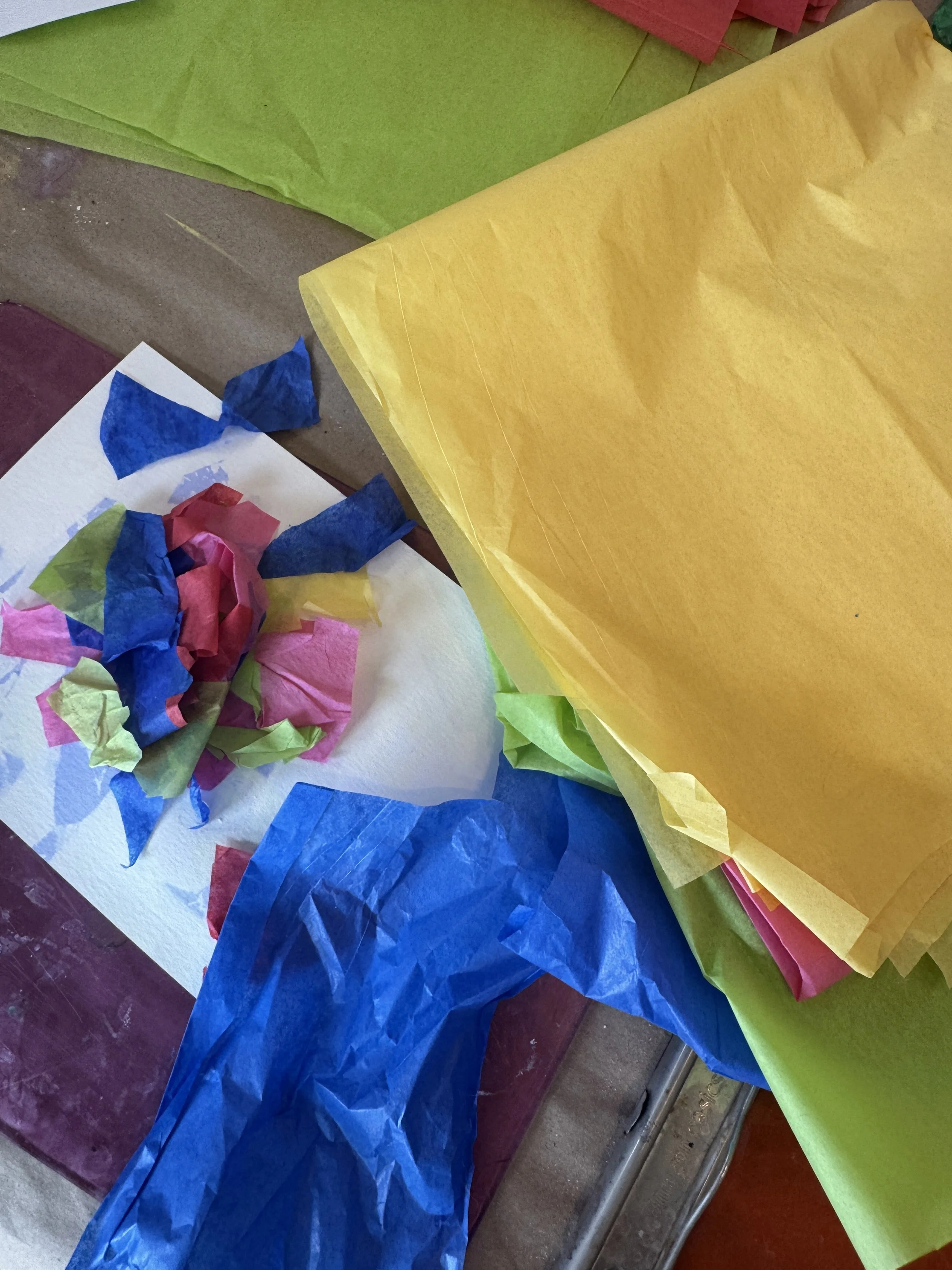 Colorful tissue papers in green, yellow, red, pink, blue, and purple, with some crumpled, on a table.